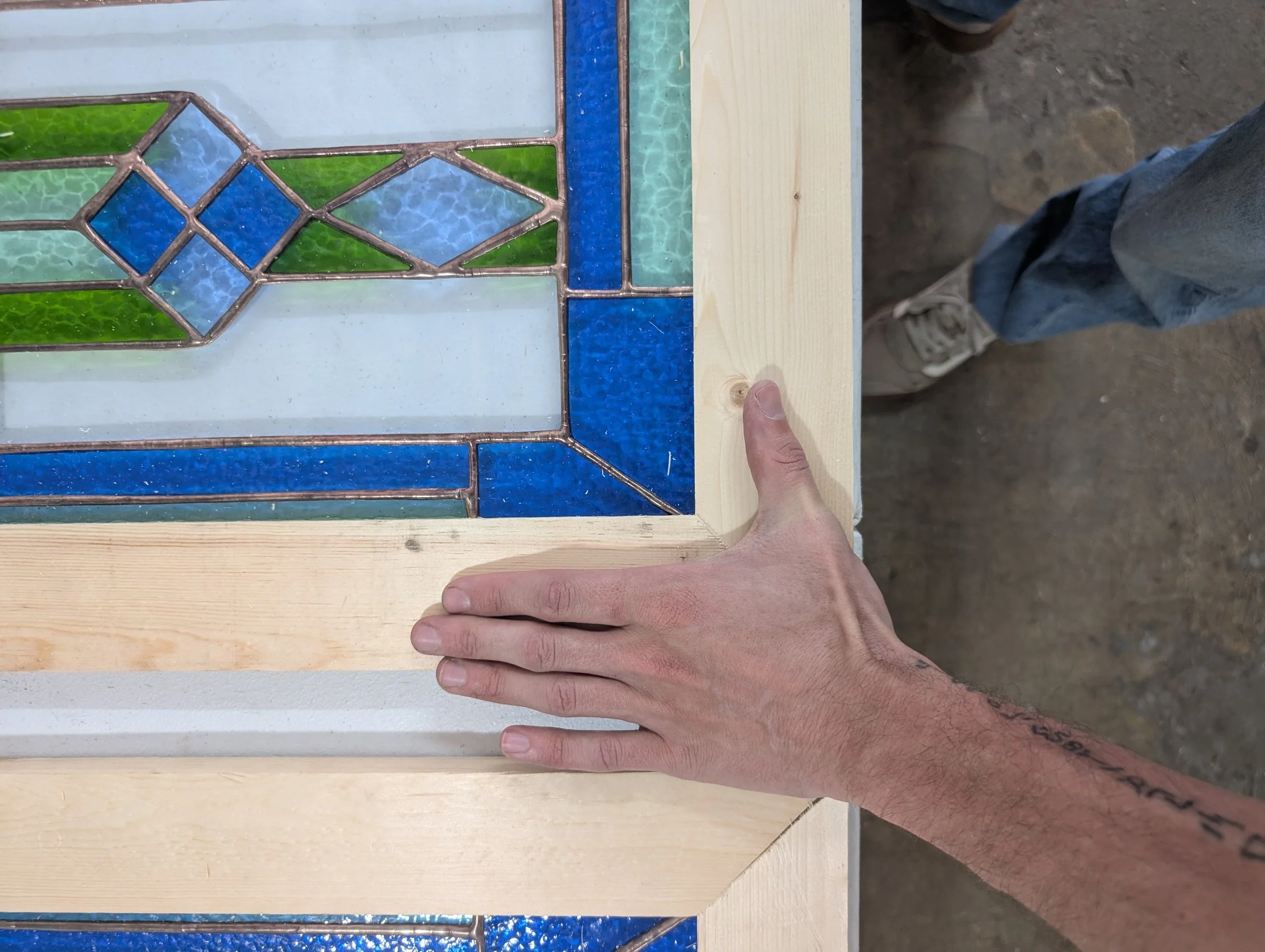 Person installing stained glass window frame with a wooden border.