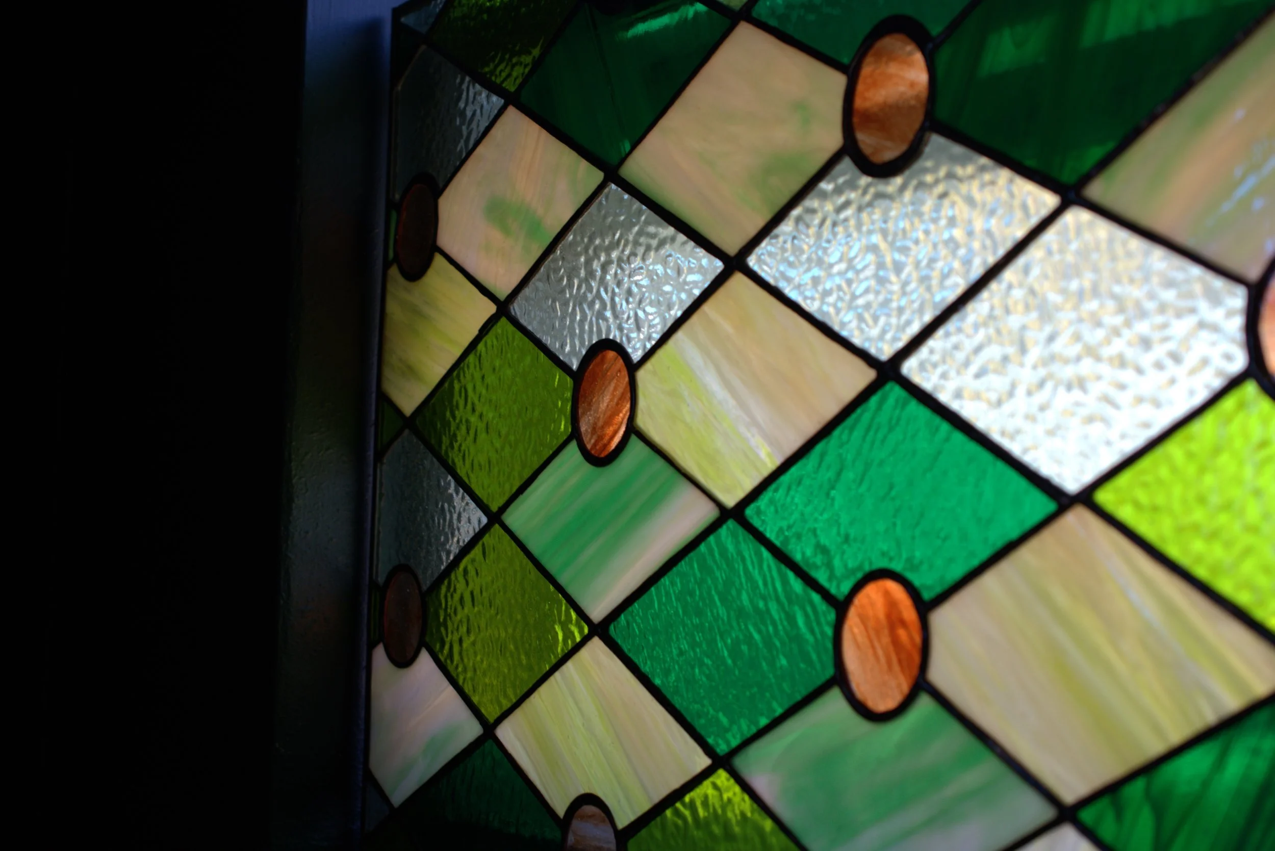 Close-up of a colorful stained glass window with green, white, and amber panels arranged in a geometric pattern.
