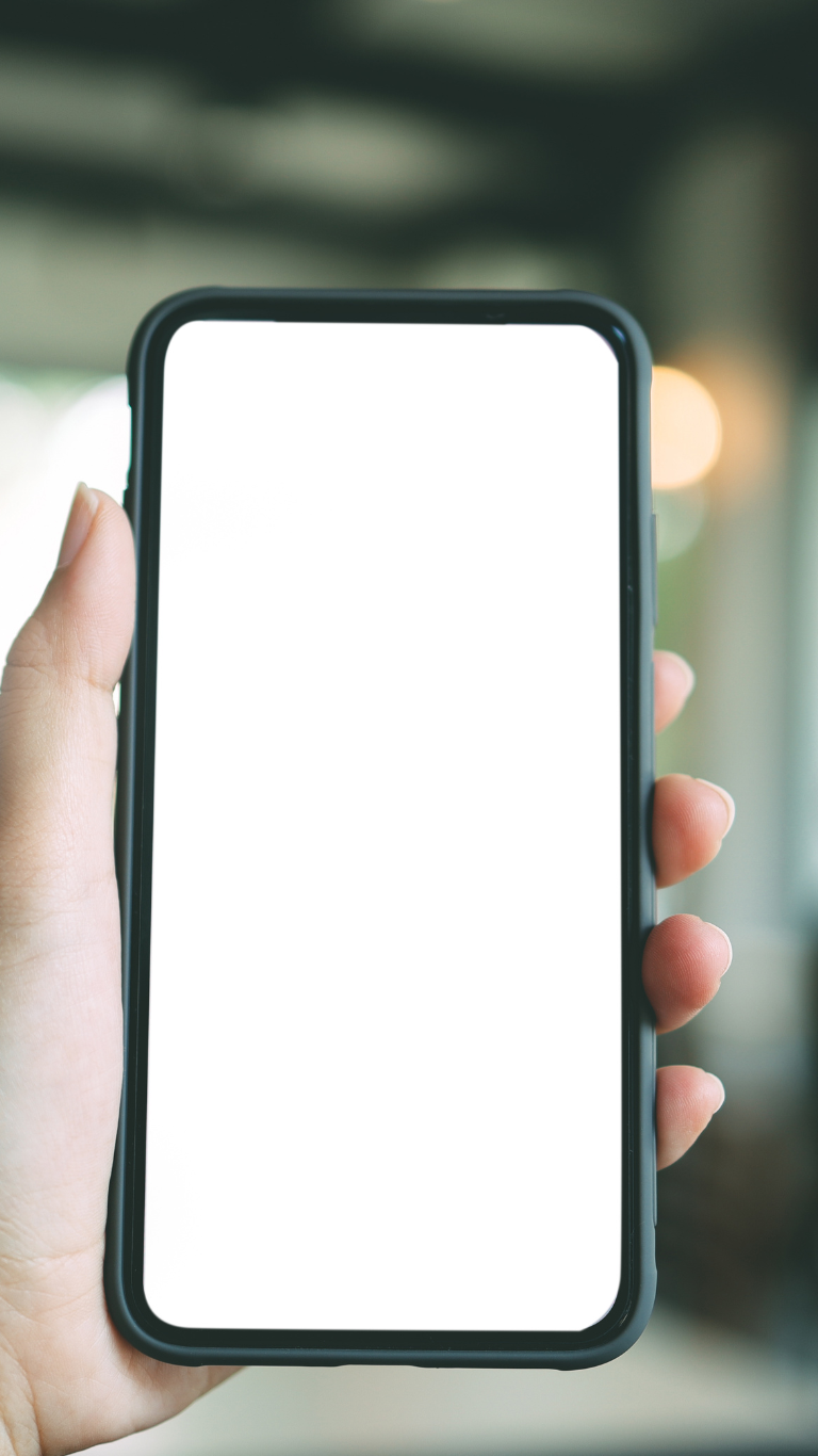 Person holding a smartphone with a blank white screen indoors.