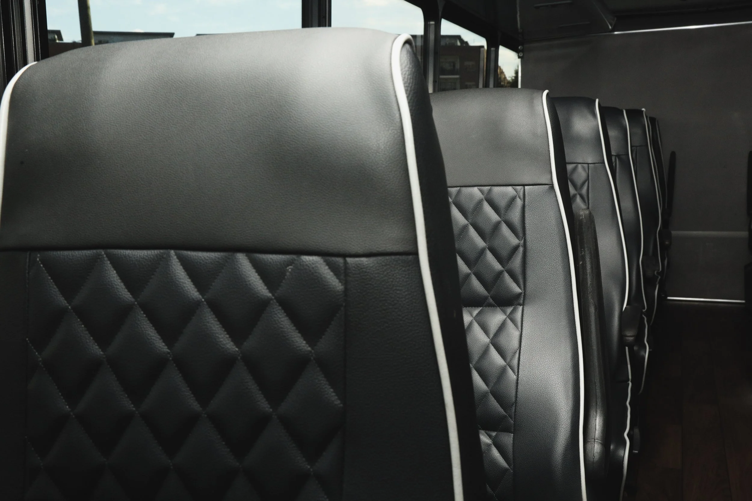 Row of black leather bus seats with quilted backs and white piping.