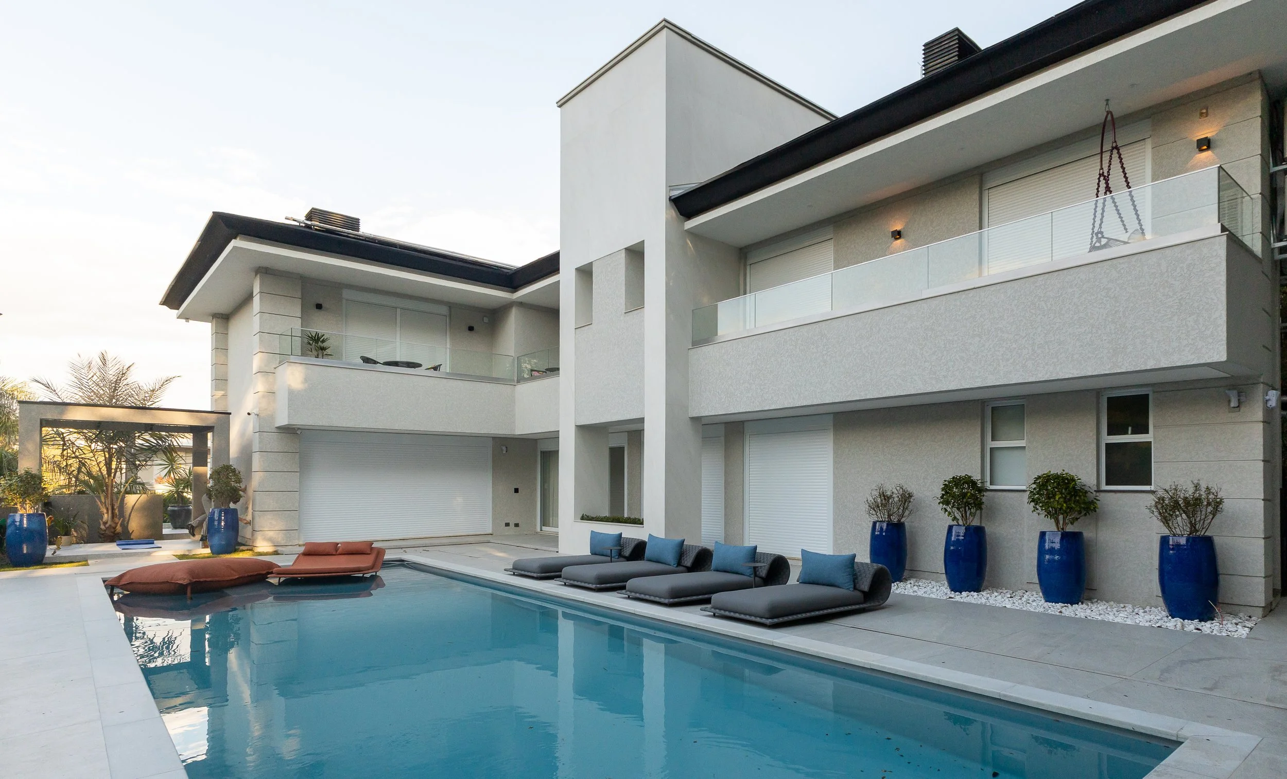 Residência moderna com varanda e piscina ao ar livre, espreguiçadeiras e vasos azuis com plantas.