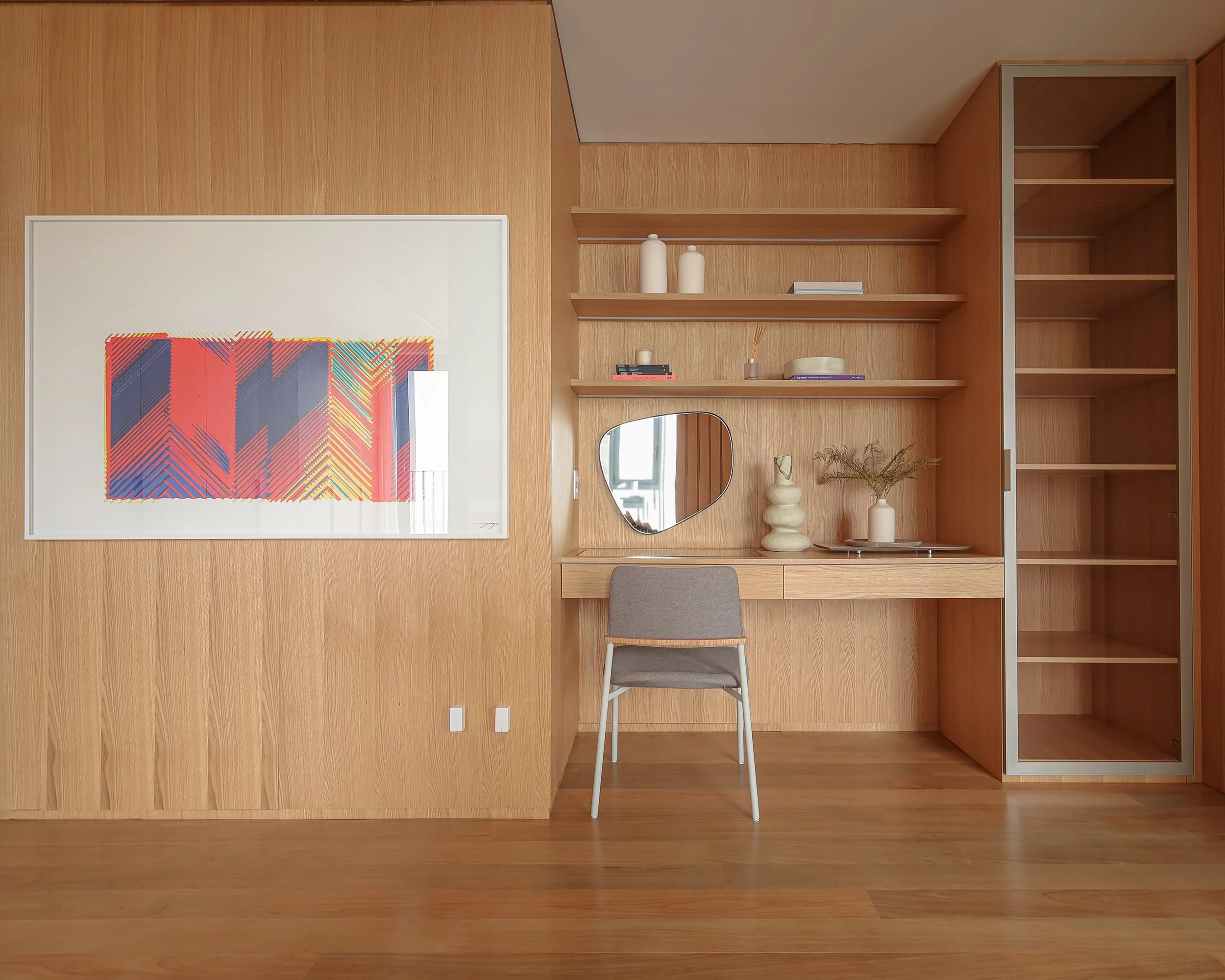 Interior com paredes de madeira, um espelho, uma cadeira, prateleiras com objetos decorativos, e uma parede com uma obra de arte