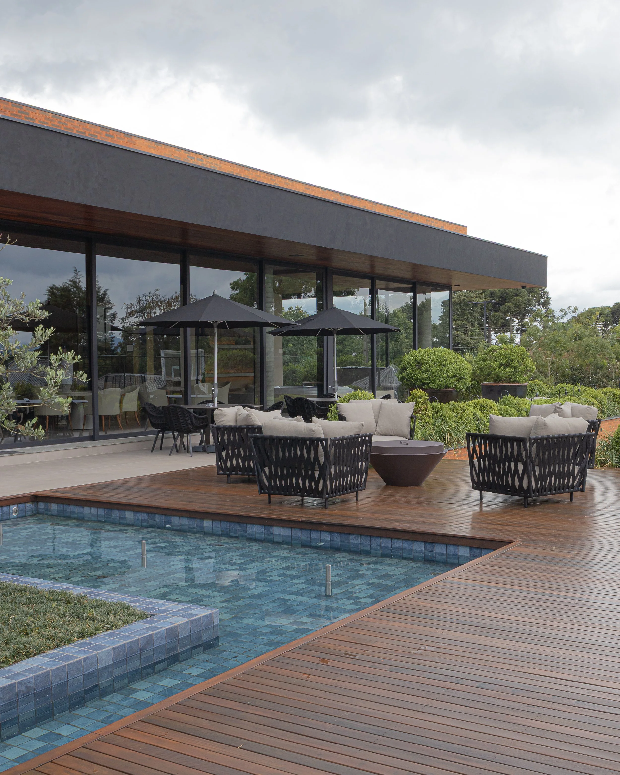 Área de lazer com piscina, móveis de jardim e uma casa moderna com paredes de vidro
