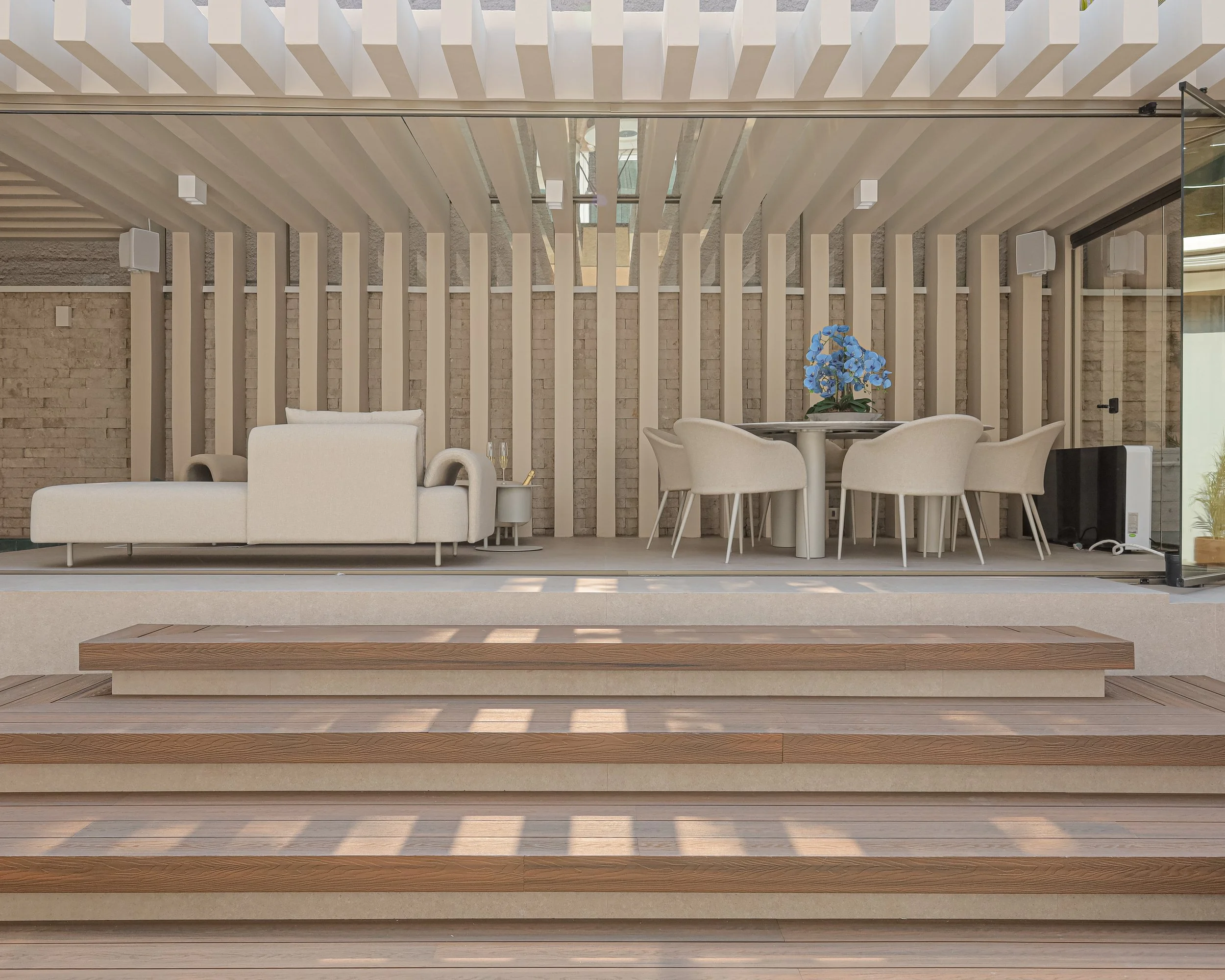 Sala de estar moderna com móveis brancos, mesa de jantar com cadeiras e vaso de flores azuis, piso de madeira e fundo de parede de tijolos.