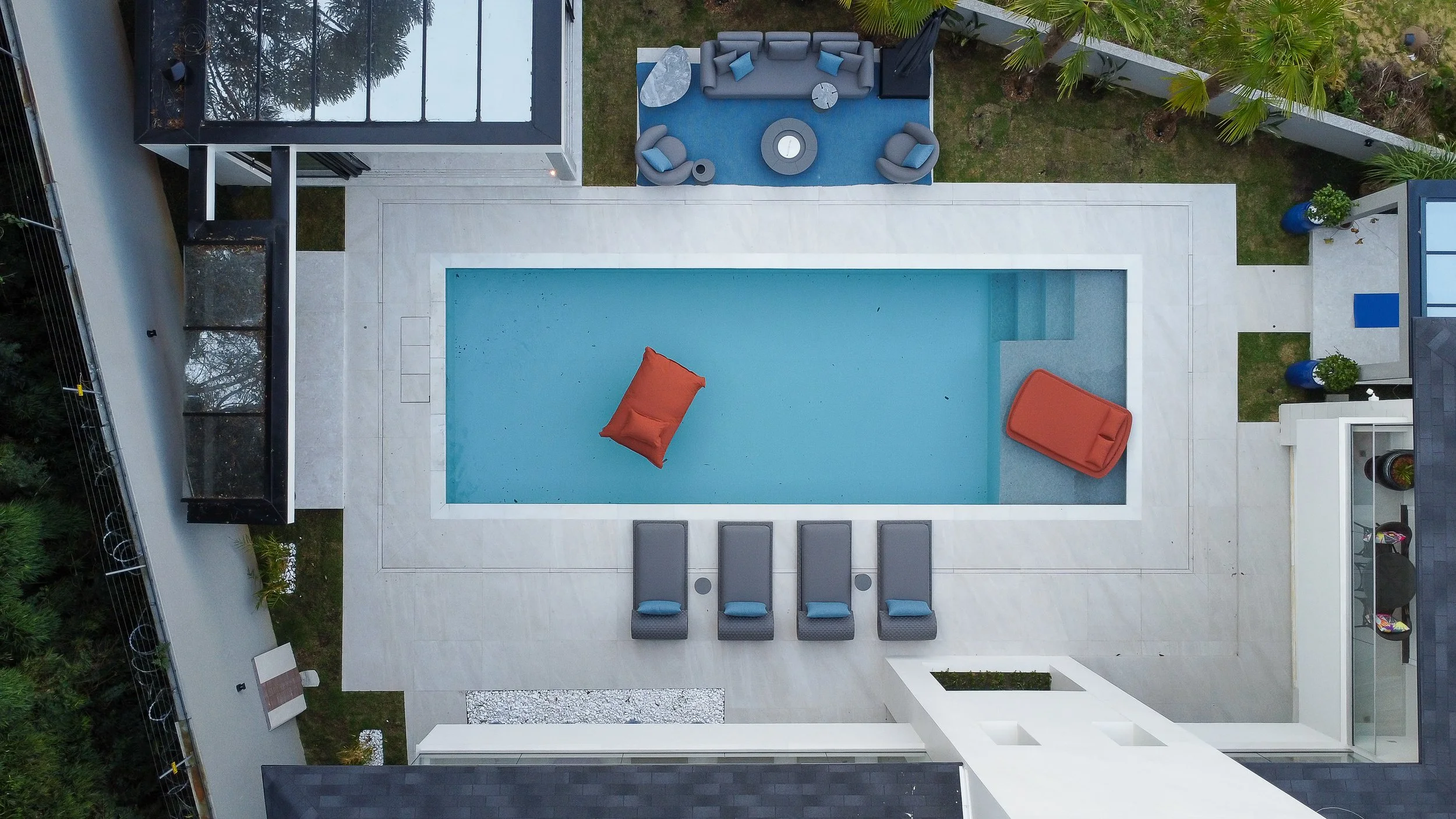 Imagem de uma piscina ao ar livre com cadeiras e espreguiçadeiras ao redor, vista de cima.