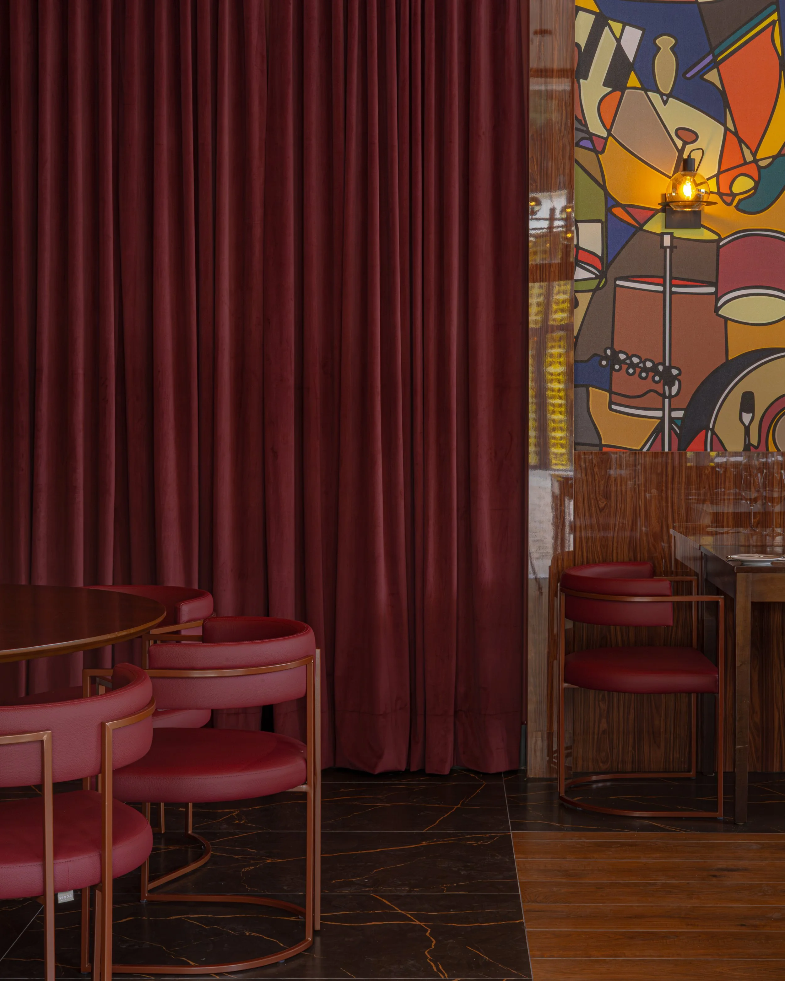 Interior de um restaurante com cortinas vermelhas, parede com mural colorido de instrumentos musicais e poltronas vermelhas com estrutura de metal.