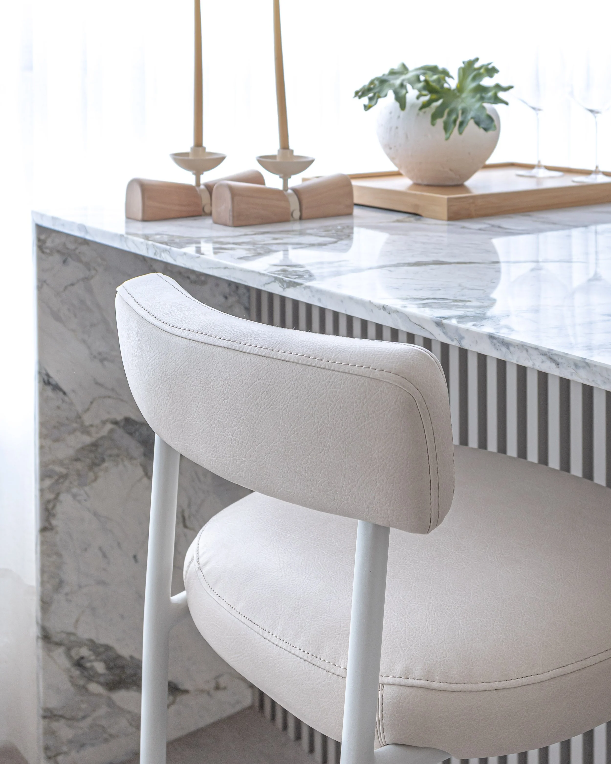 Sofá ou cadeira branca com estrutura de metal, próximo a uma mesa de mármore com decoração.