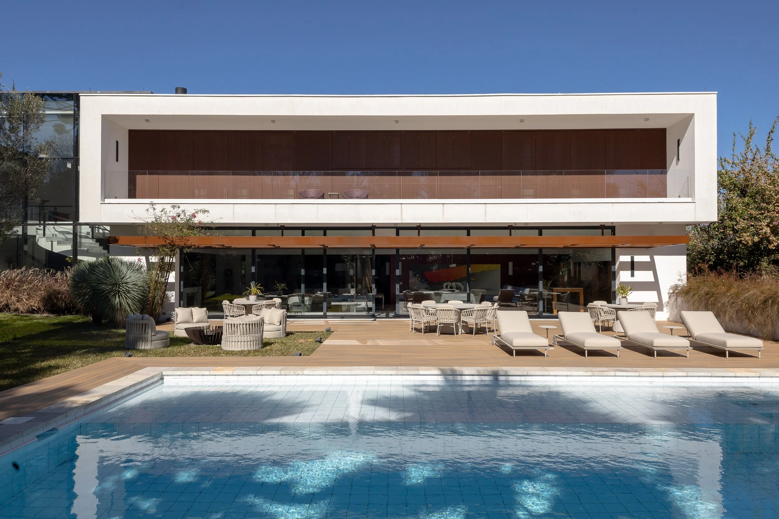 Edifício moderno com varanda e piscina ao ar livre, espreguiçadeiras e área de estar ao redor.