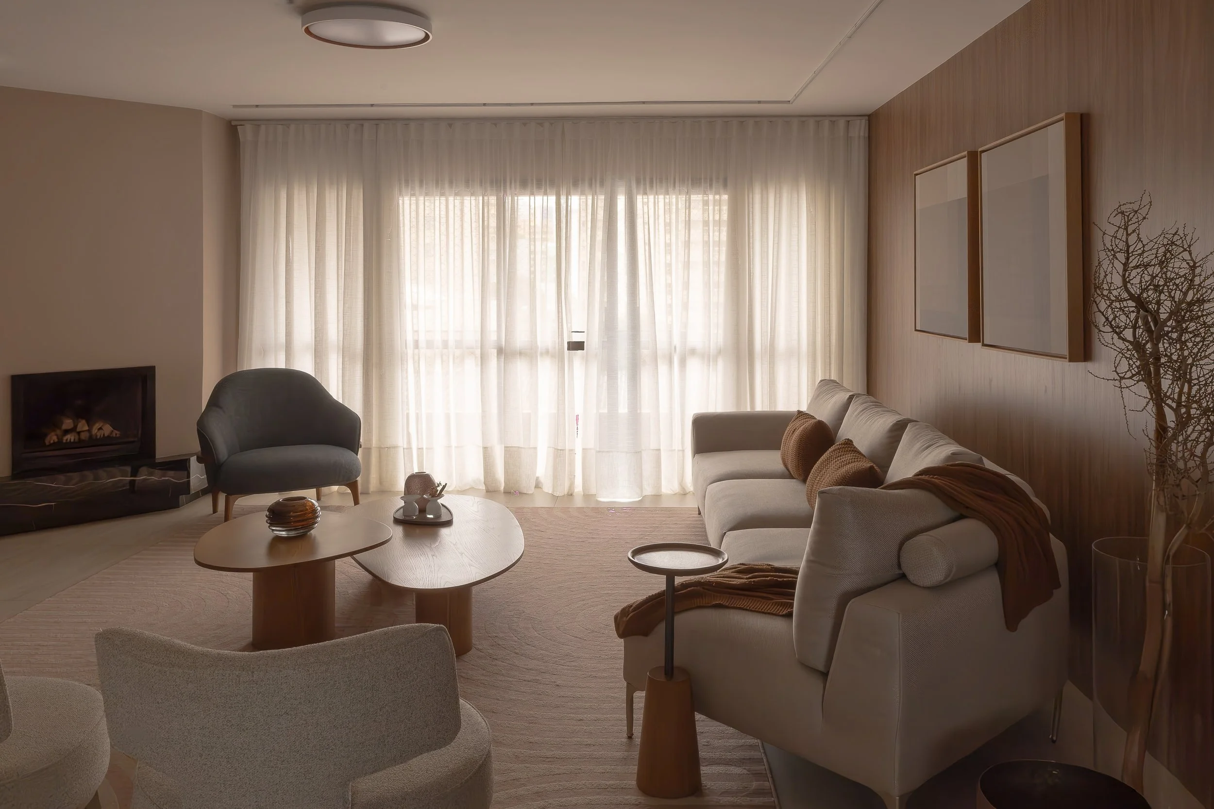 Sala de estar com sofá bege, poltrona cinza, mesa de centro de madeira, cortinas claras, parede de madeira, vitro com quadro branco, vaso com planta seca