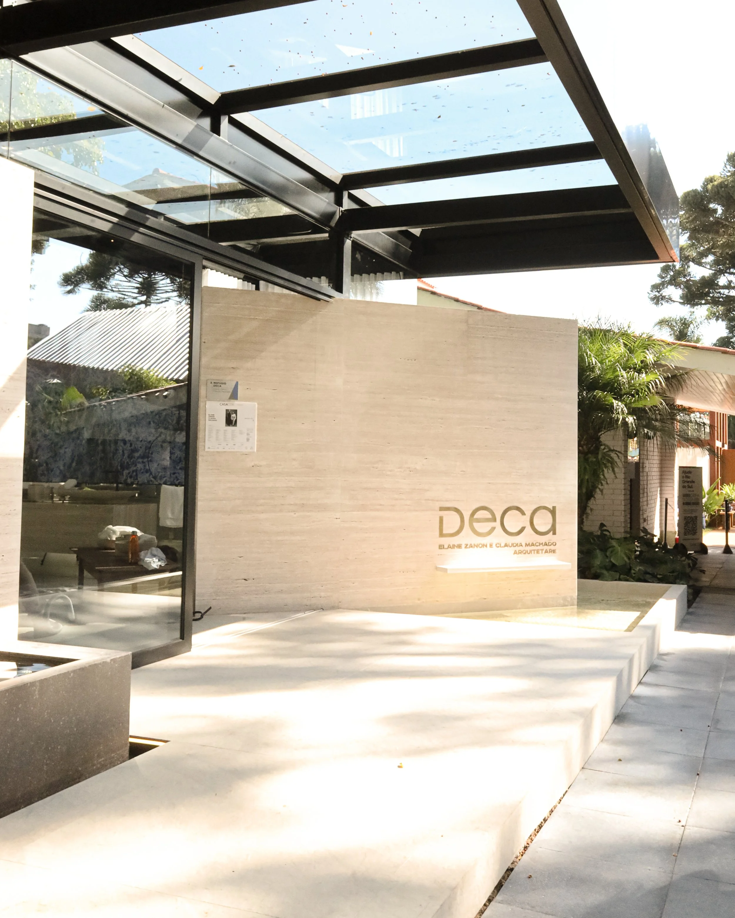 fachada moderna de edifício com parede de pedra e letreiro de metal com o nome 'deca', sob uma estrutura de vidro e metal