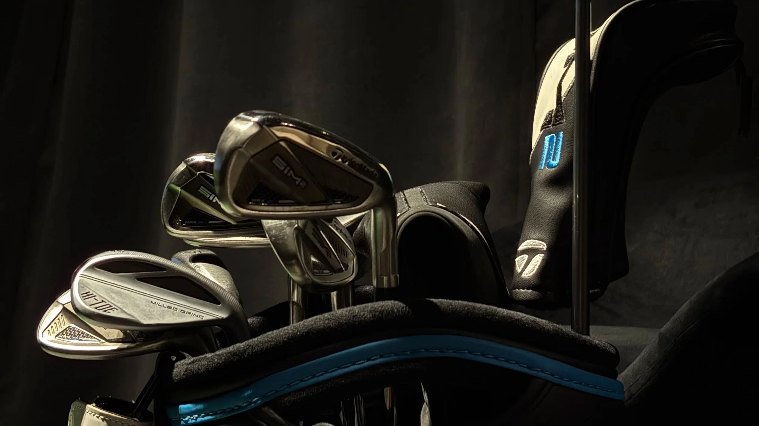 Golf clubs in a golf bag, including irons and a putter, against a dark background.