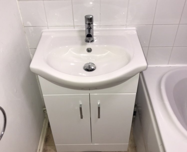 A white bathroom vanity with a small sink and a chrome faucet, positioned between a wall and a bathtub.
