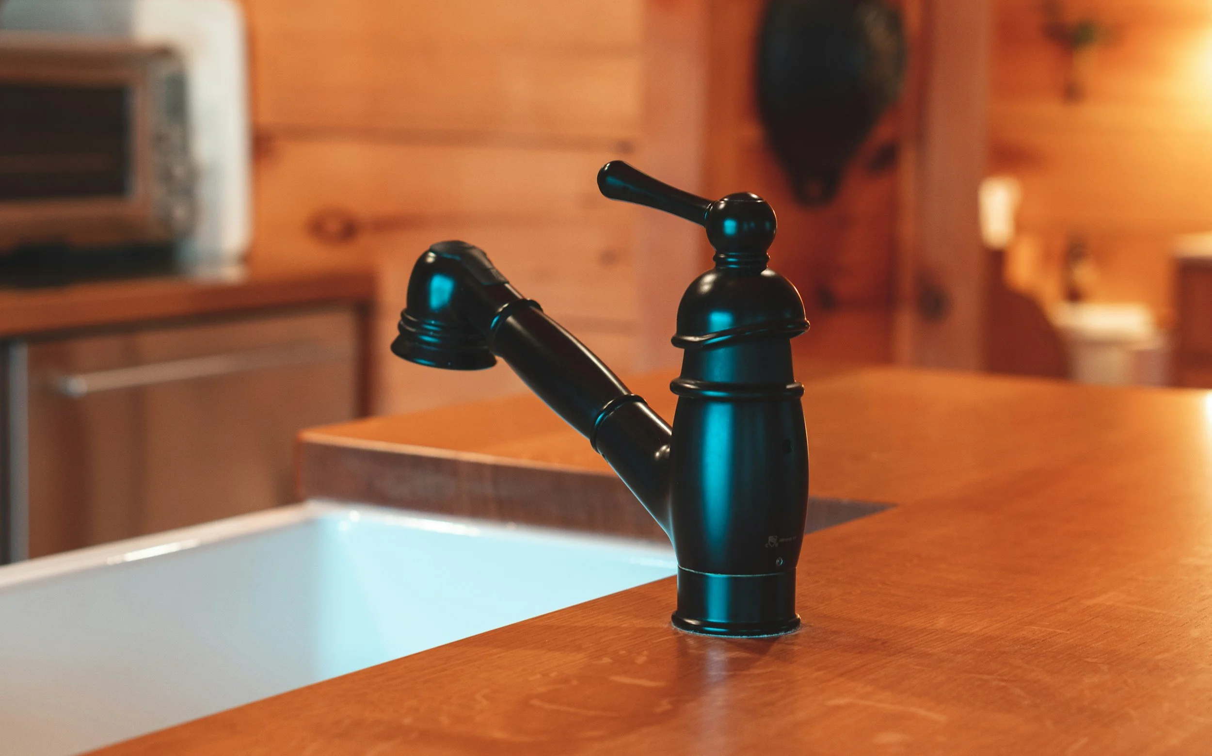 Black kitchen faucet on a wooden countertop in a cozy wooden kitchen.