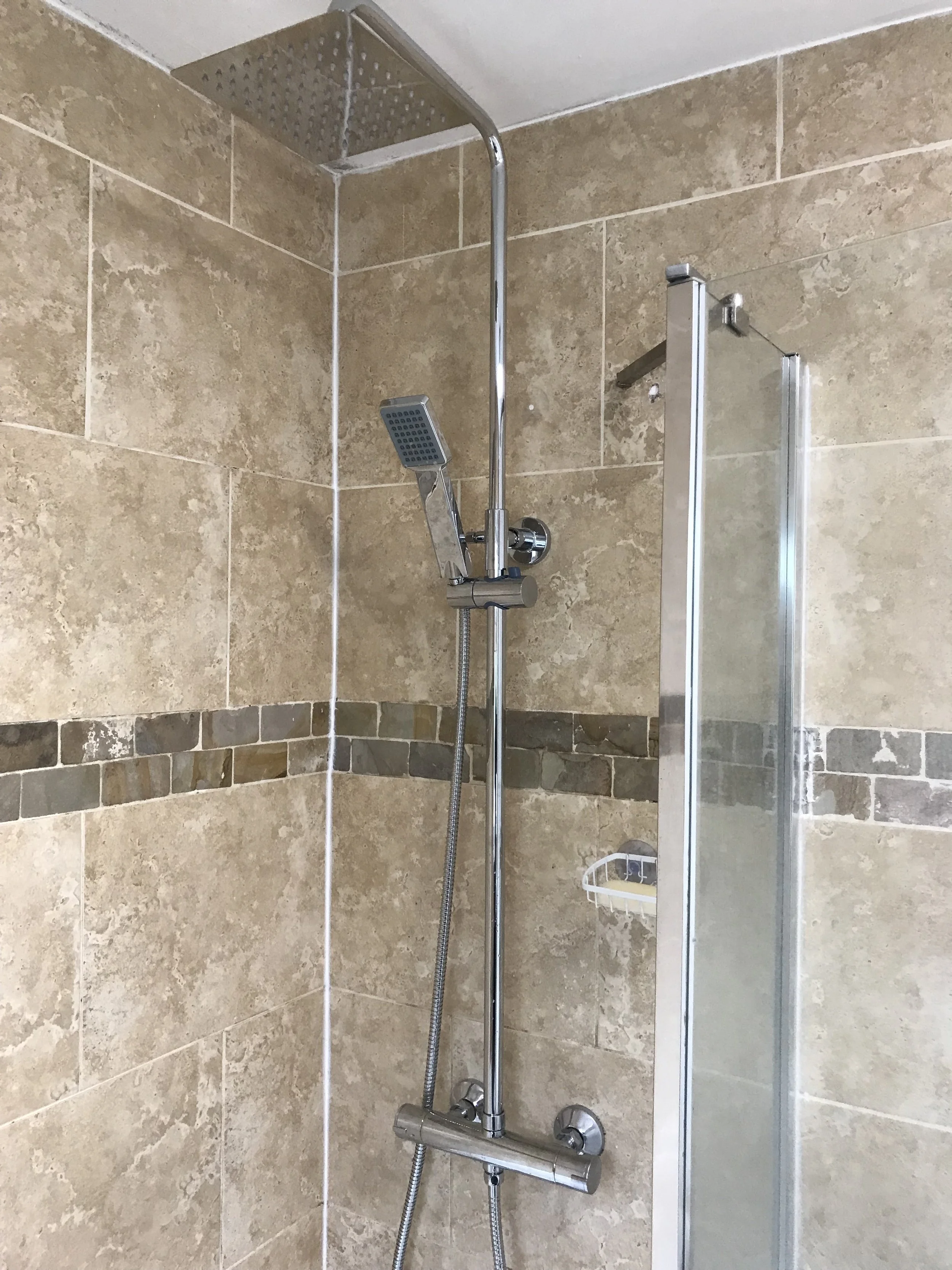 A shower with beige tile walls, a rainfall showerhead at the top, a hand-held showerhead on an adjustable rail, and a glass partition on the right side.