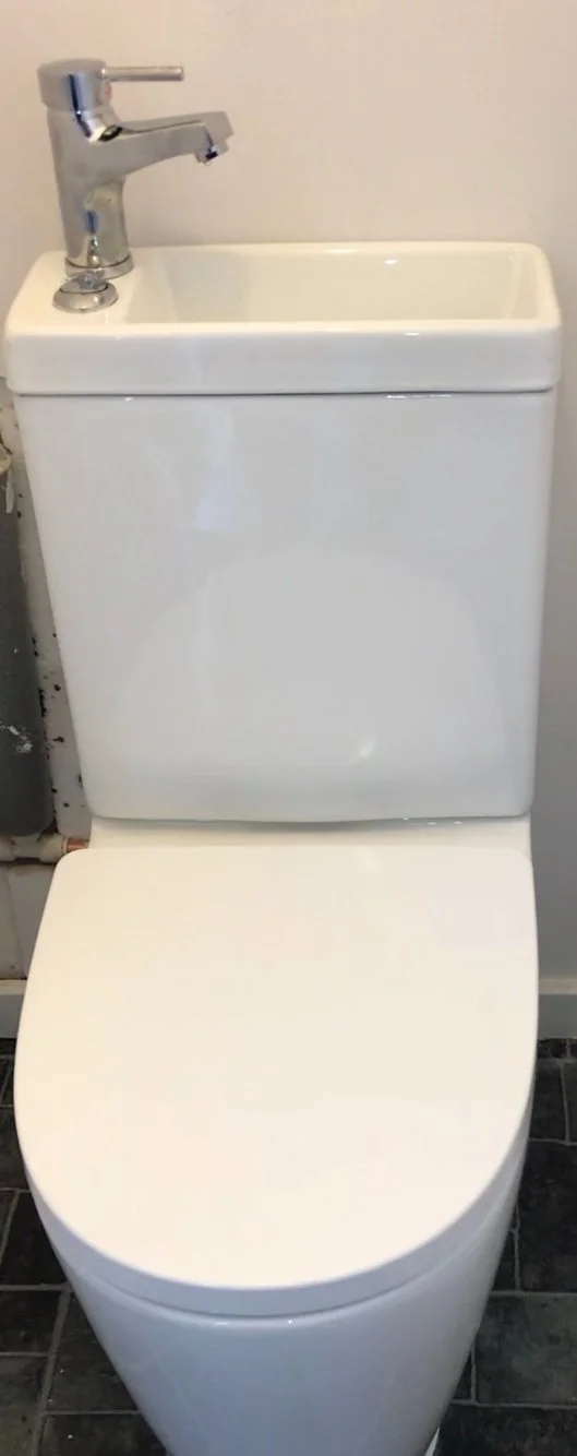 A white toilet with a tank that has an integrated sink and faucet on top.