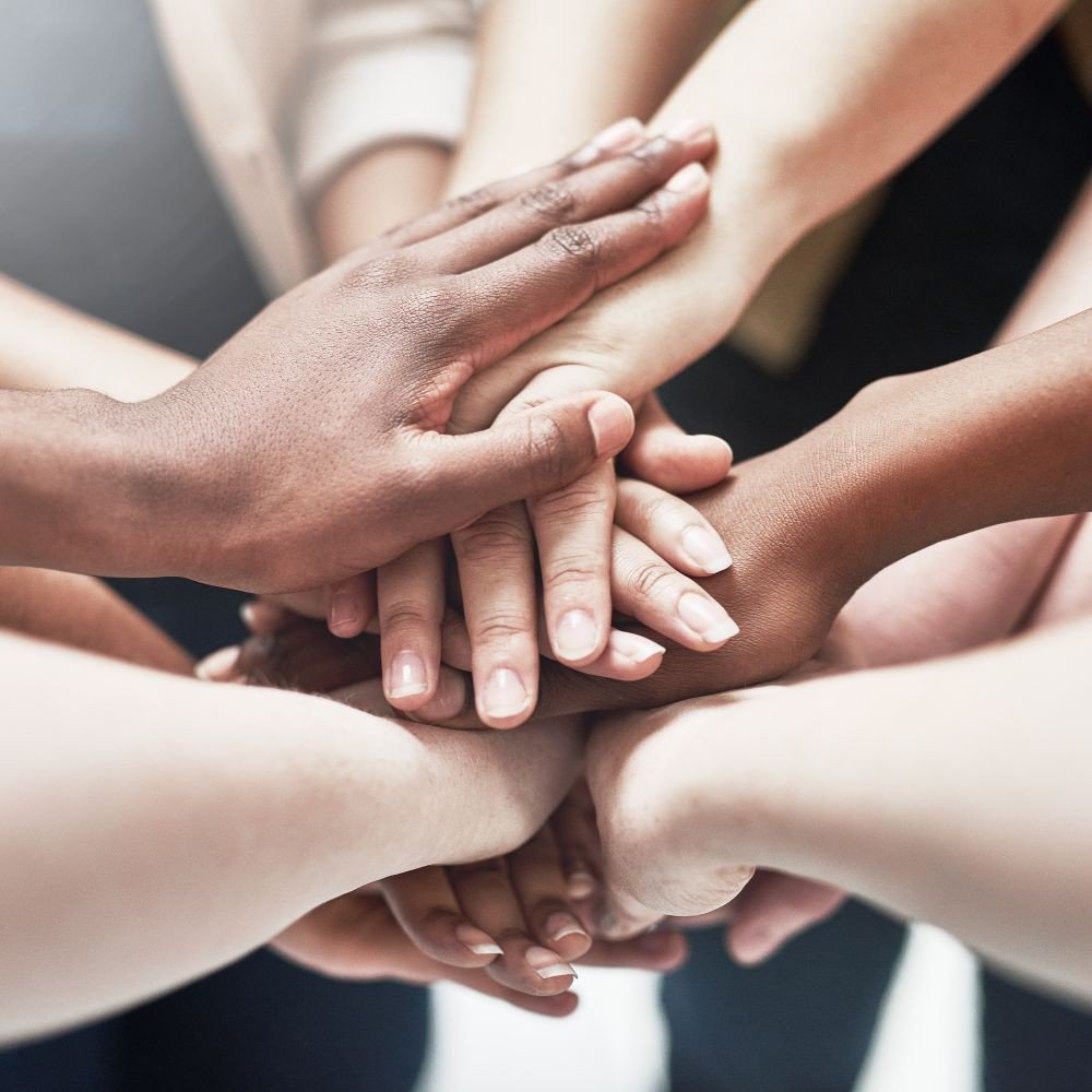 Multiple hands of diverse skin tones stack on top of each other in a show of unity and teamwork.