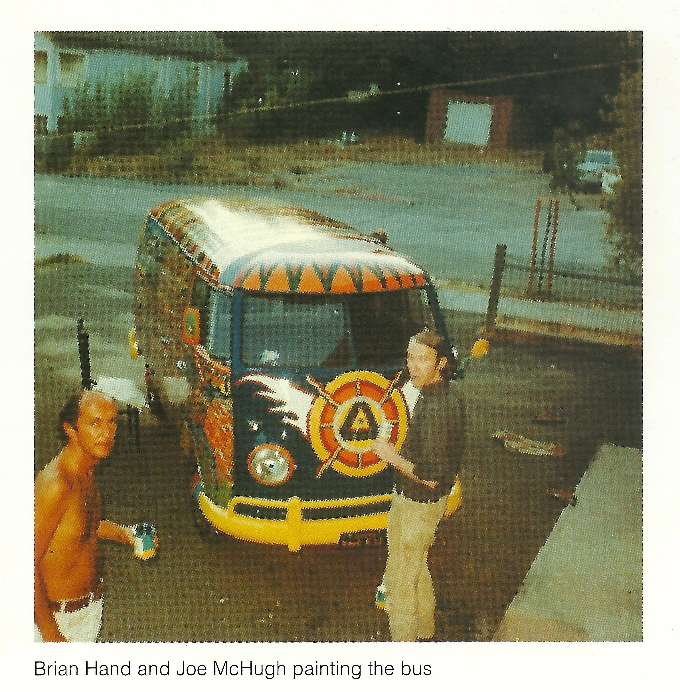 Brian Hand and Joe McHugh painting a colorful bus with psychedelic and tribal designs, parked outdoors on a street.