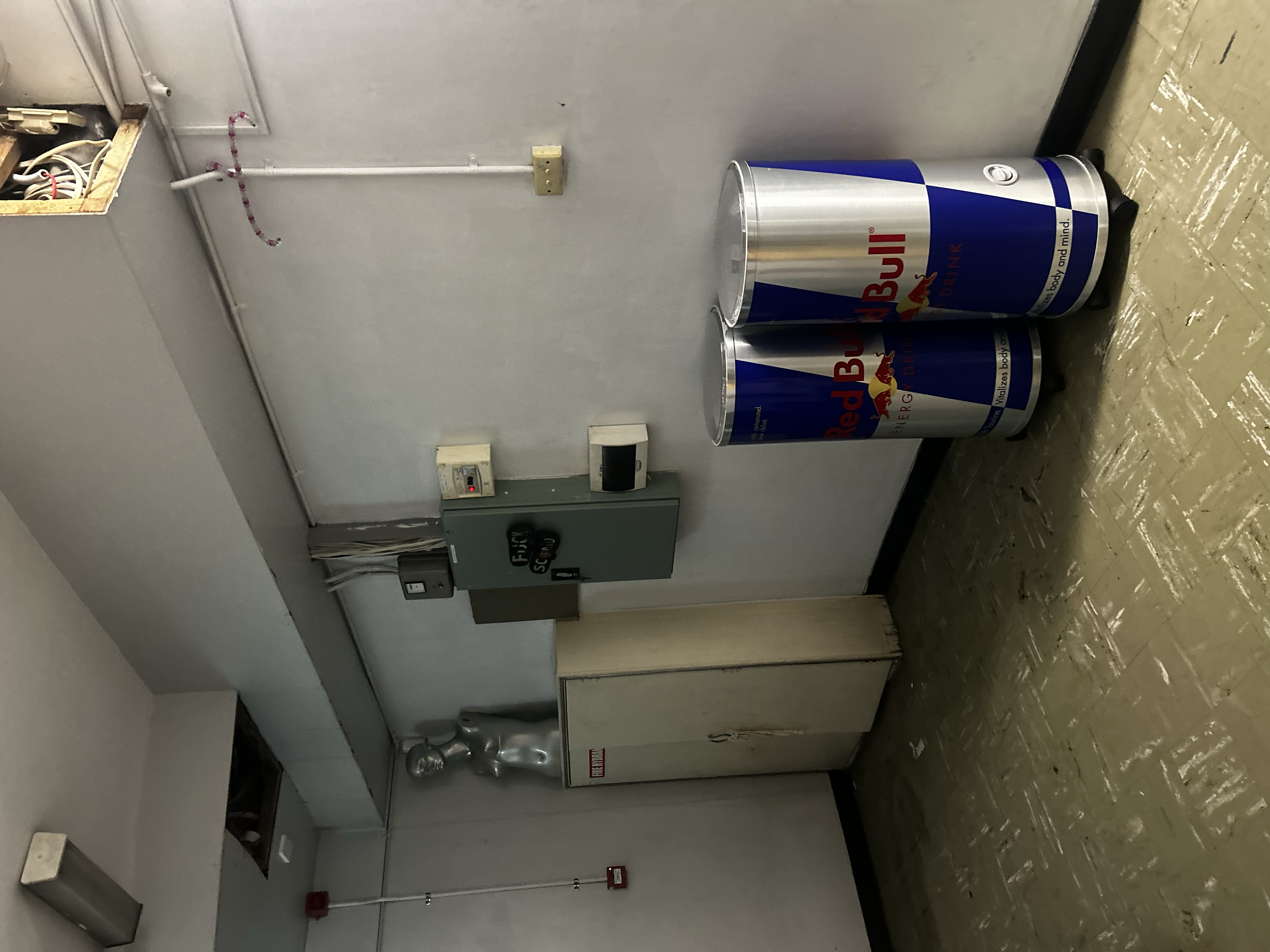Two cans of Red Bull energy drink placed on the floor next to a wall in an indoor setting.