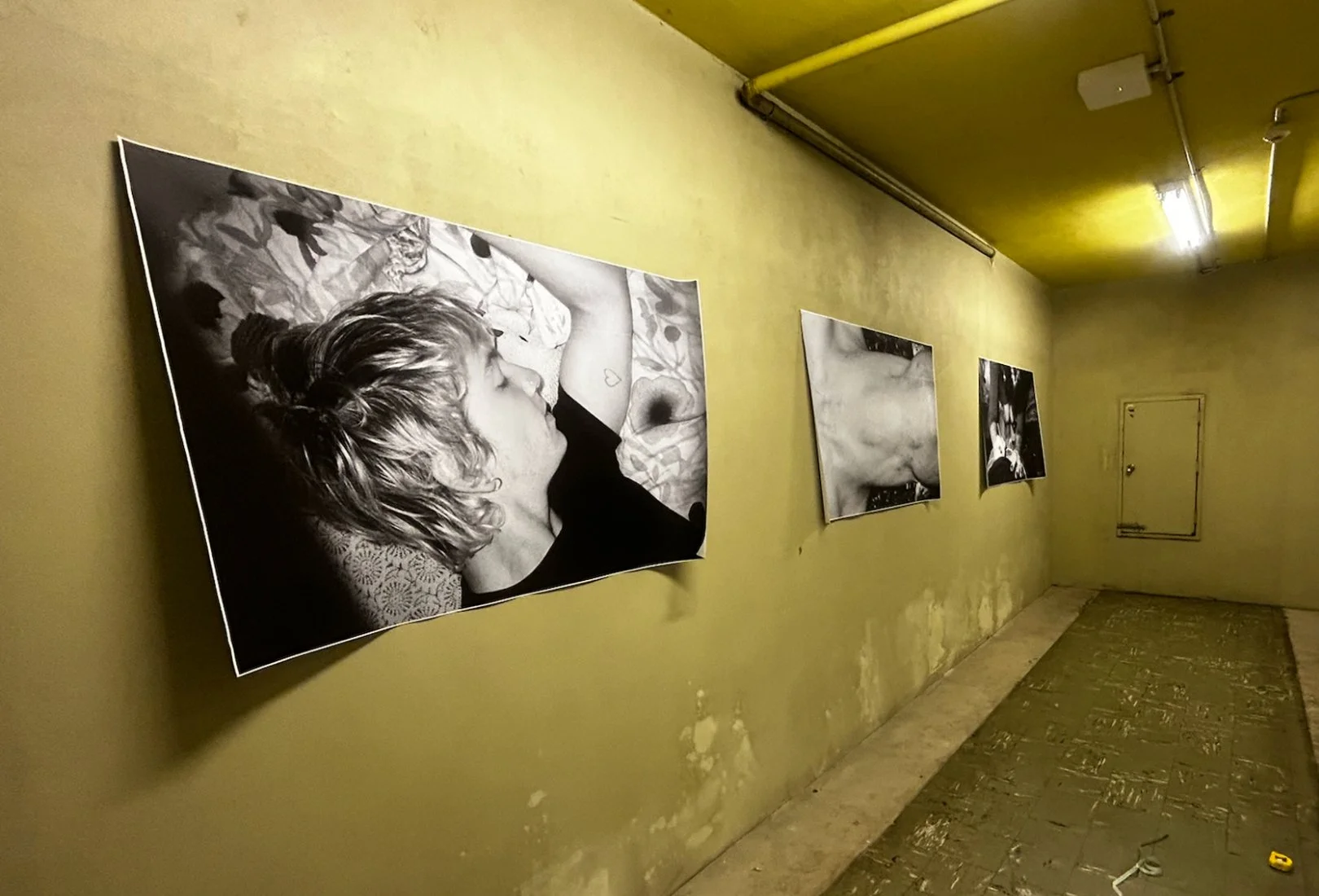 Black and white photographs of various close-up facial details displayed on a yellow wall in an art gallery or exhibition space.