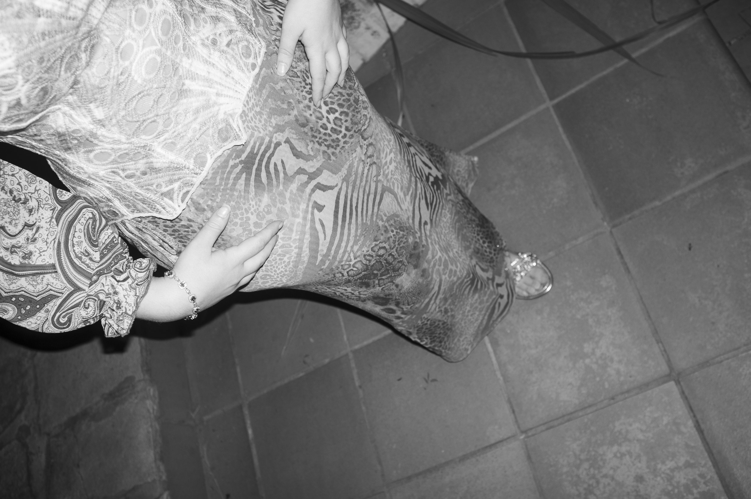 A person is standing on a tiled floor, wearing patterned pants and sandals, with hands resting on the pants.