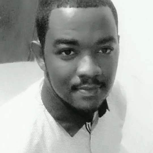 Portrait d'un homme jeune en noir et blanc, portant un pull clair, regardant l'appareil photo avec un léger sourire.