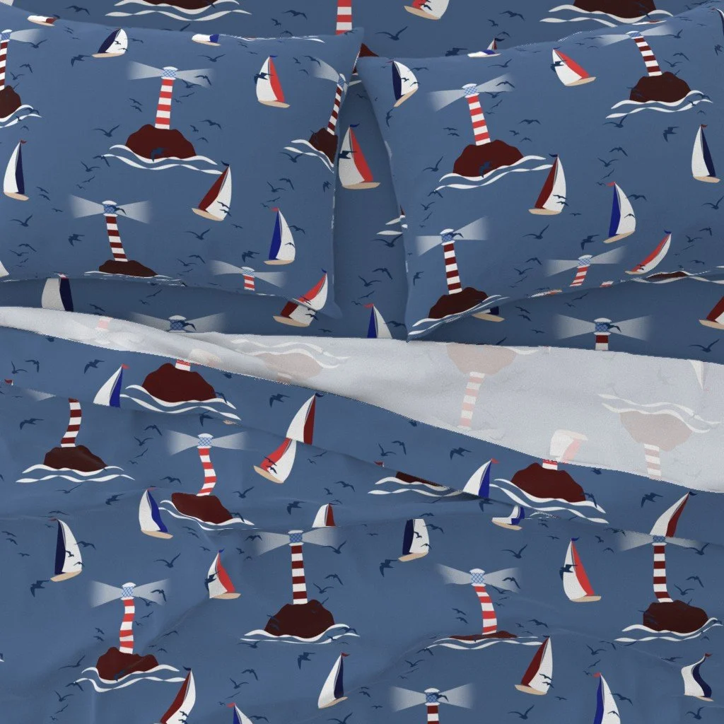 Sail Away Storybook Collection by Aitch Jay Designs — blue lighthouse and sailboat repeat with gentle waves and seabirds, shown on coastal bedding to create a soft maritime bedroom aesthetic.