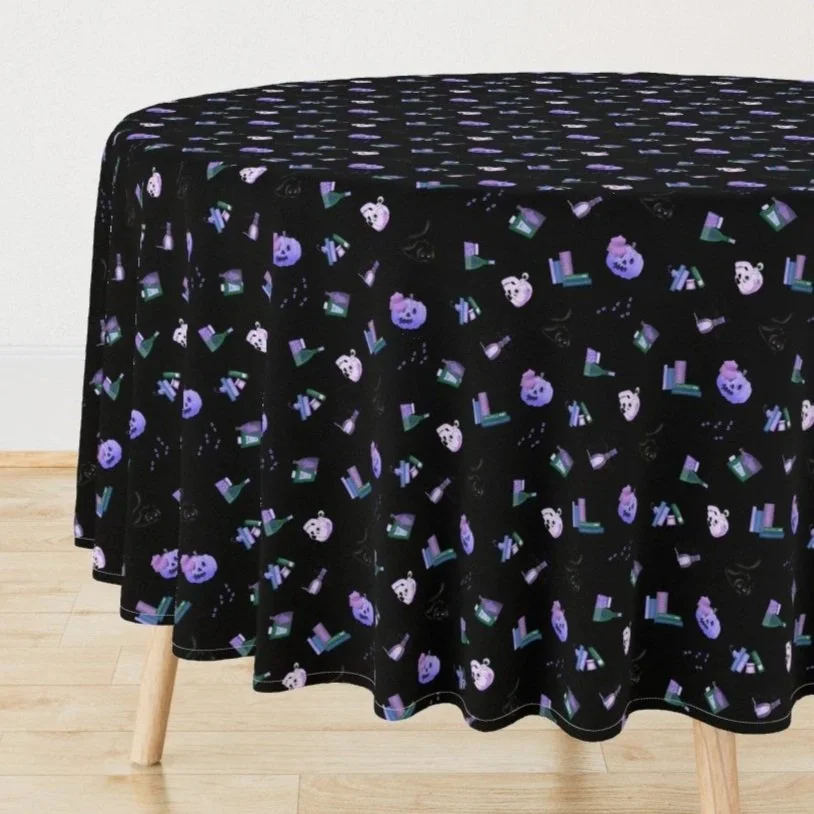 Table covered with a black tablecloth featuring a pattern of purple and white cartoon faces, books, and medical bottles, set on a wooden floor with a plain white wall background.