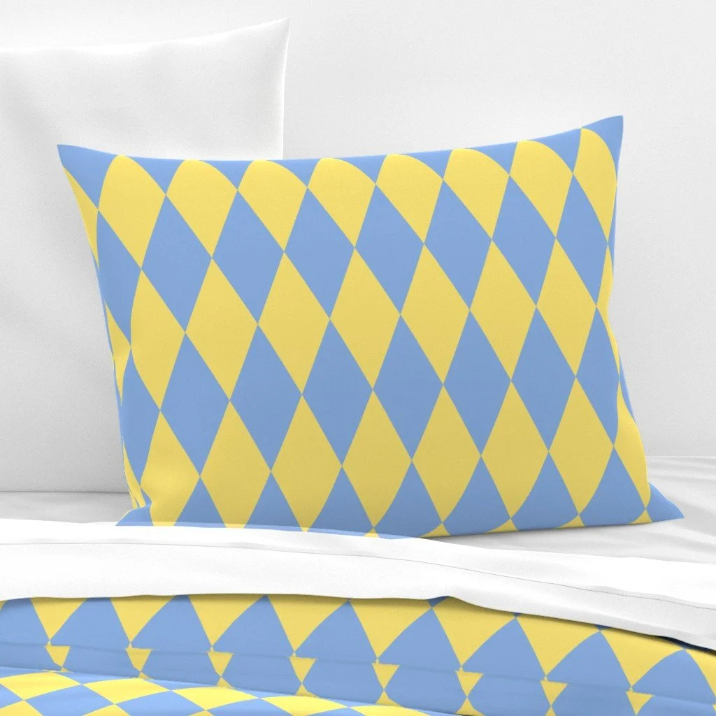 A pillow with a blue and yellow diamond pattern on a bed with white bedding.