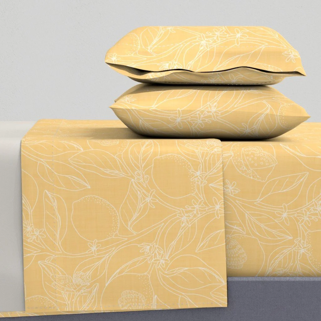 Two pillows with a yellow and white floral pattern rest on a matching yellow and white floral tablecloth.