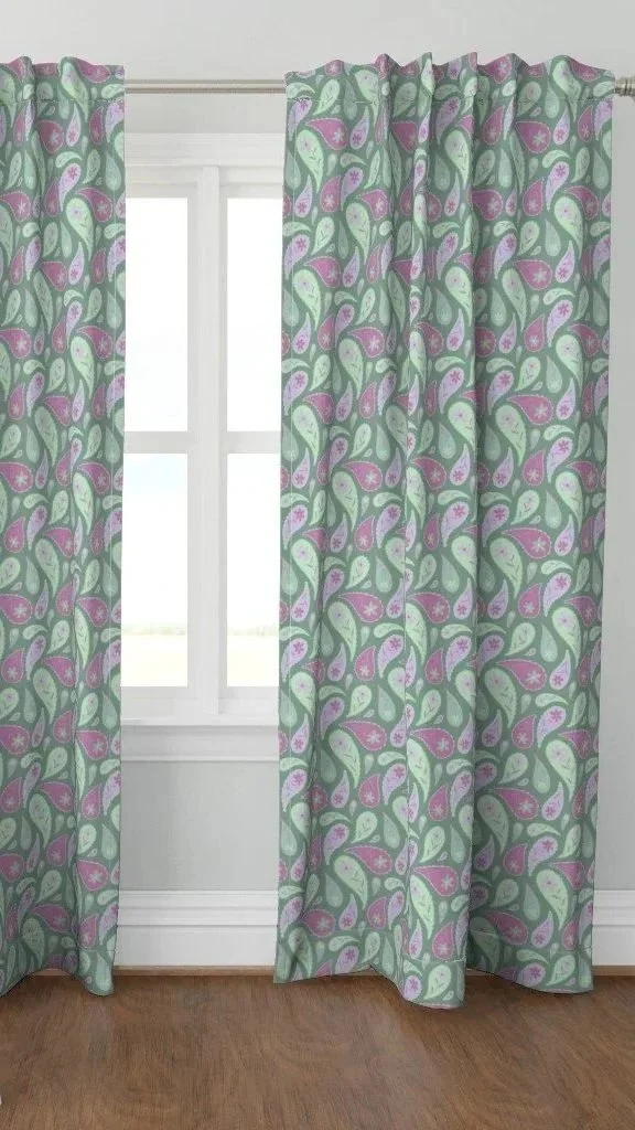 Colorful patterned curtains with green, purple, and lavender leaf design hanging in front of a window in a room with light-colored walls and wood floor.
