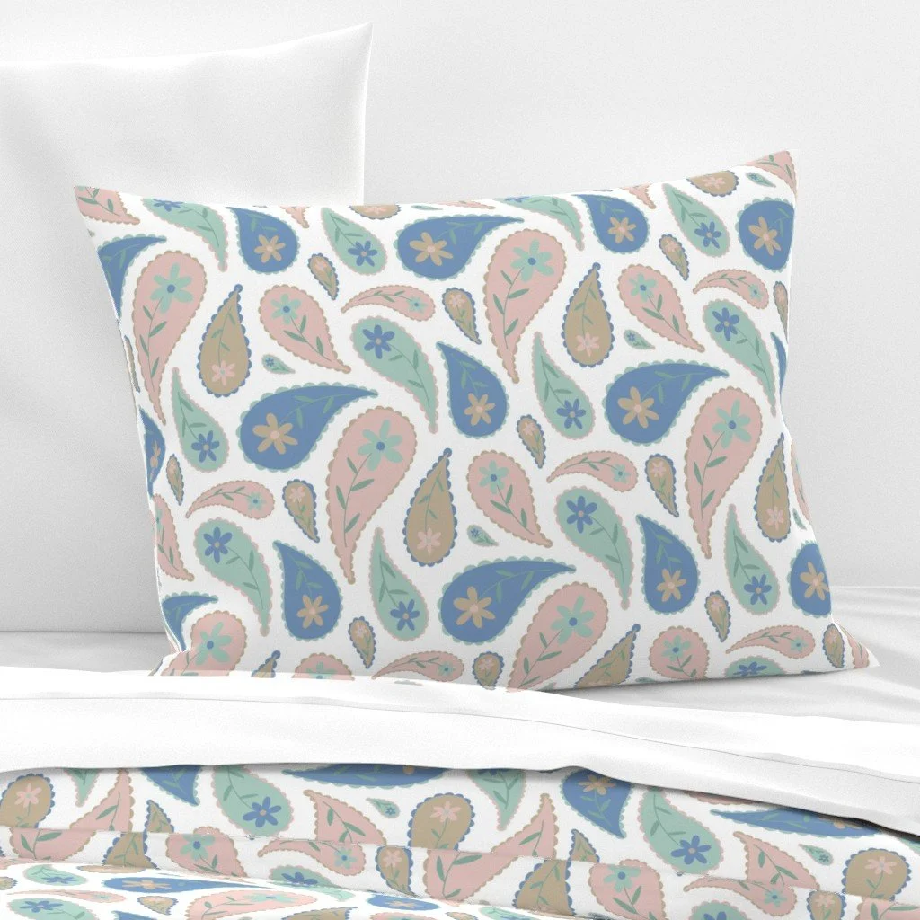 Decorative pillow with a paisley pattern in blue, pink, green, and beige on a white bed with plain white sheets and pillowcases.