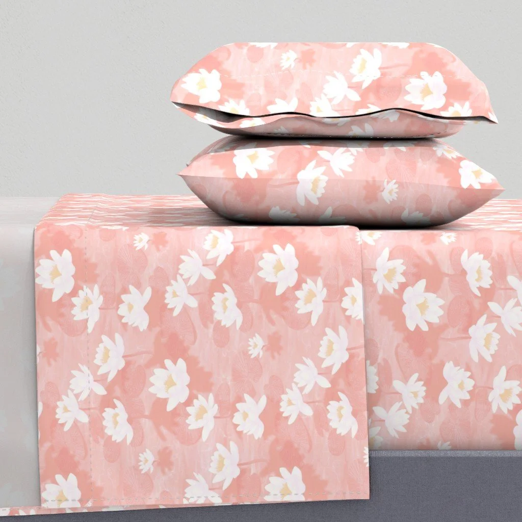 Lotus Blossom Drift by Aitch Jay Designs — a soft coral pink floral repeat featuring white lotus blooms, shown on bedding to emphasise the calm, serene design.