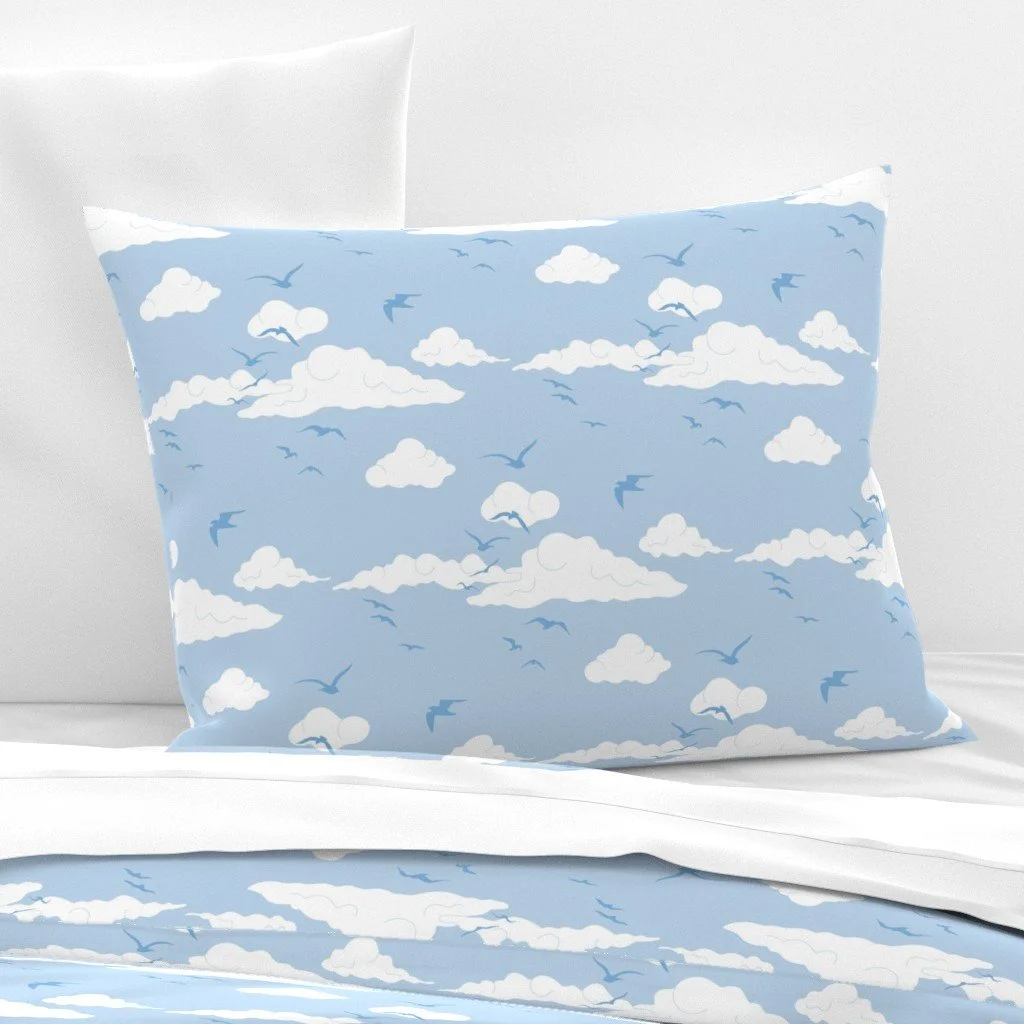 Pillow and bedsheet with a blue sky pattern featuring white clouds and flying birds.