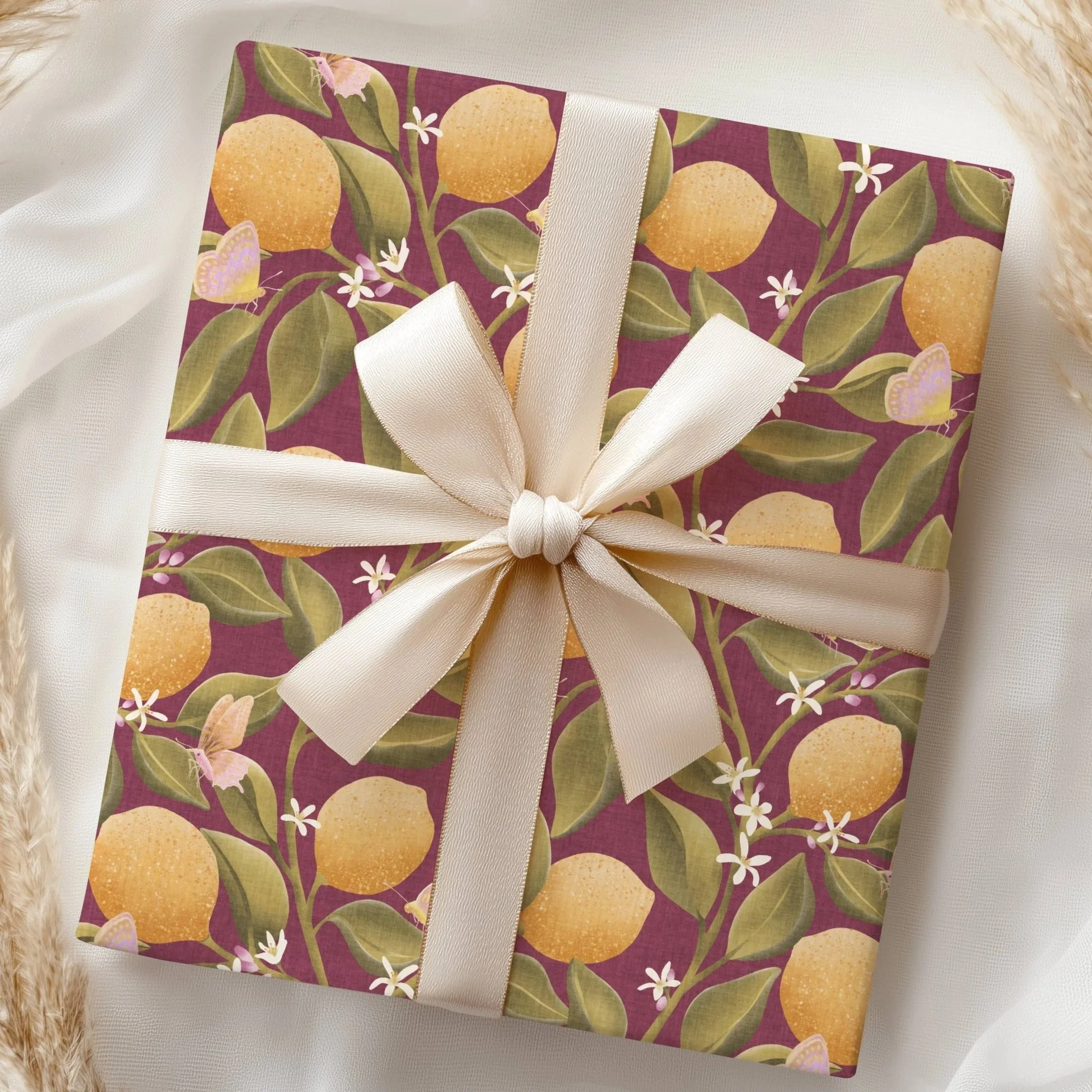 Gift wrap featuring the Lemon Tree Garden botanical pattern with hand‑drawn lemons, green leaves, blossoms, and butterflies on a warm dark red background, designed by Aitch Jay Designs.