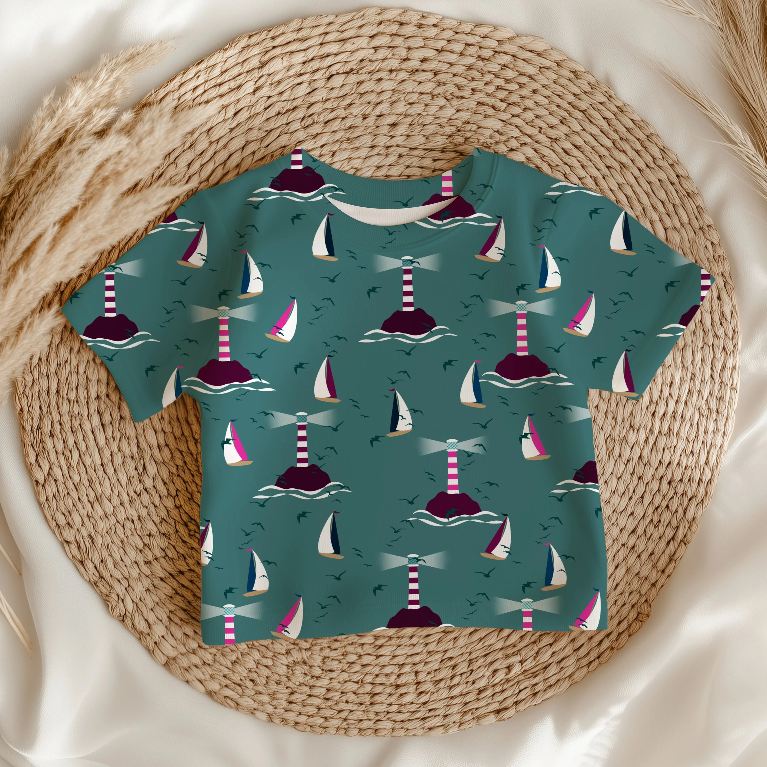 Sail Away Storybook Collection by Aitch Jay Designs — teal sailboat and lighthouse repeat with stylised waves and seabirds, shown on a children’s shirt to highlight playful coastal apparel design for kids.