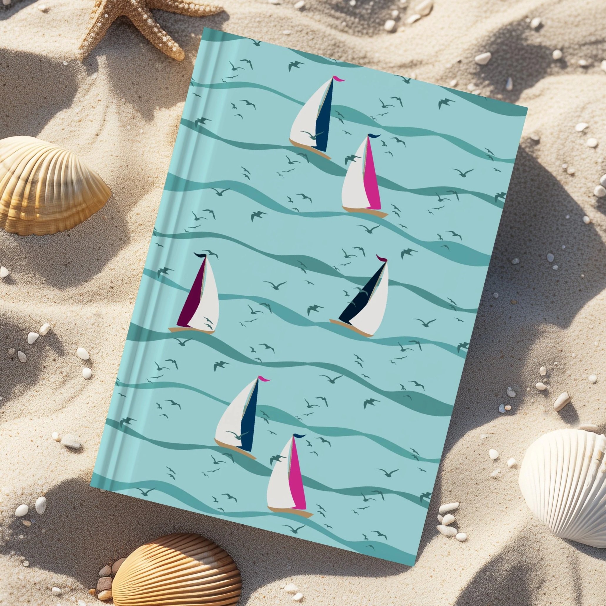 Sail Away Storybook Collection by Aitch Jay Designs — sailboat and wave repeat with soft coastal colours, shown on a notebook in a beach setting to evoke seaside travel and summer creativity.