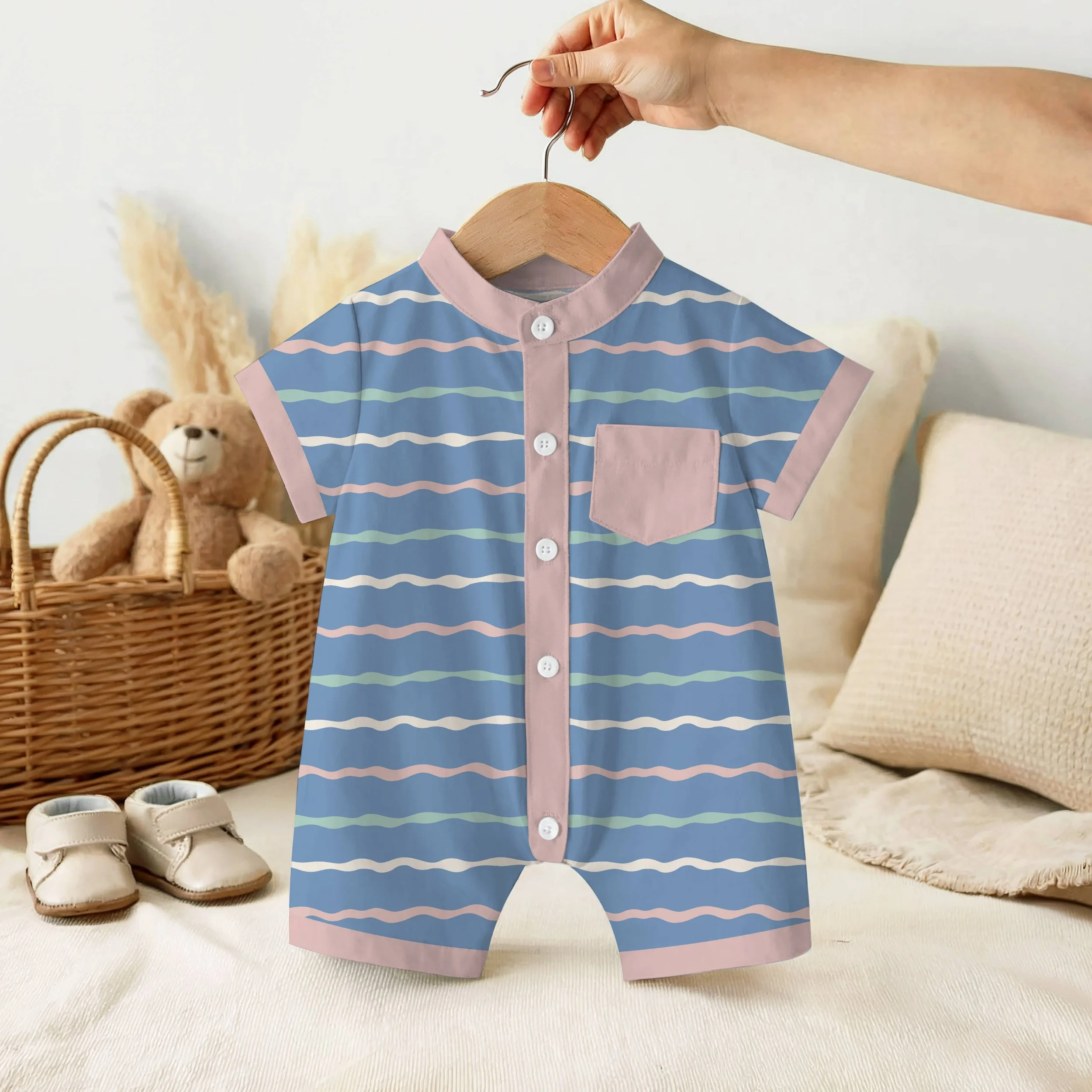 Child's shirt on a hanger with pastel pink and blue horizontal stripes, and a collar with pink trim. Surrounding items include a pair of beige shoes, a woven basket, a teddy bear, and a round woven mat.