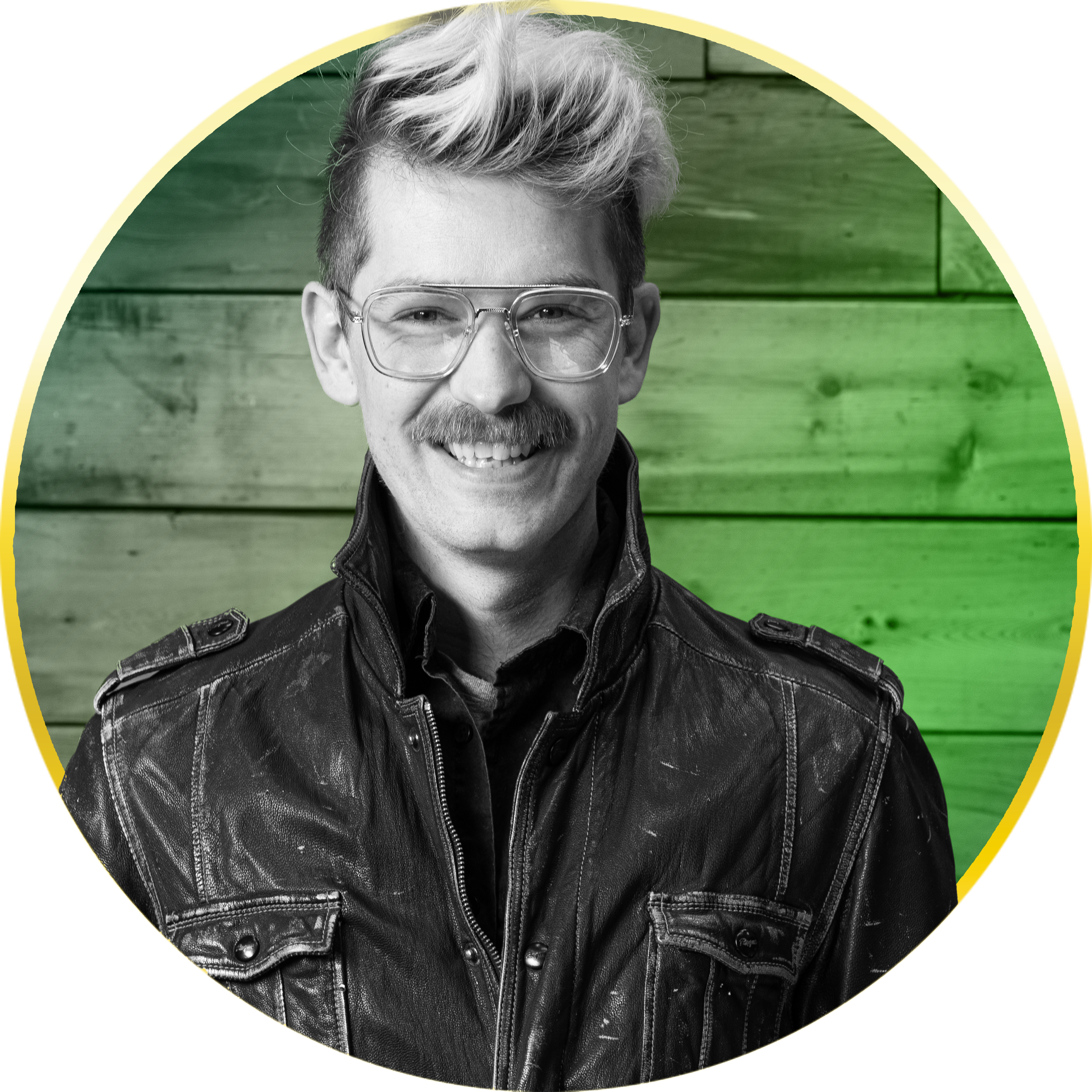 Smiling man with blonde hair, glasses, mustache, wearing a black leather jacket, standing in front of a wooden wall background.