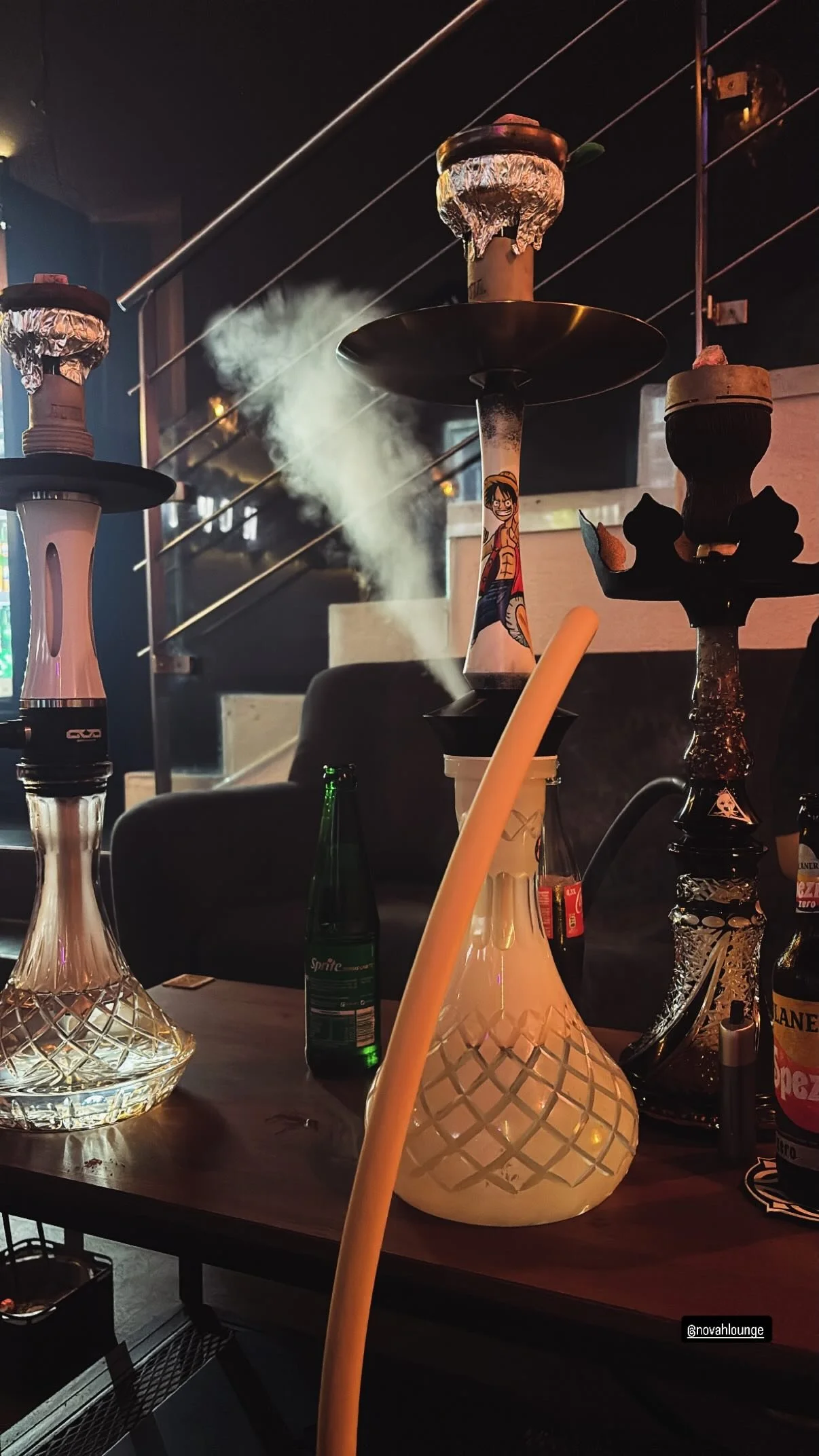 Mehrere Hookahs auf einem Tisch, Rauch steigt auf, im Hintergrund dunkel beleuchteter Raum.