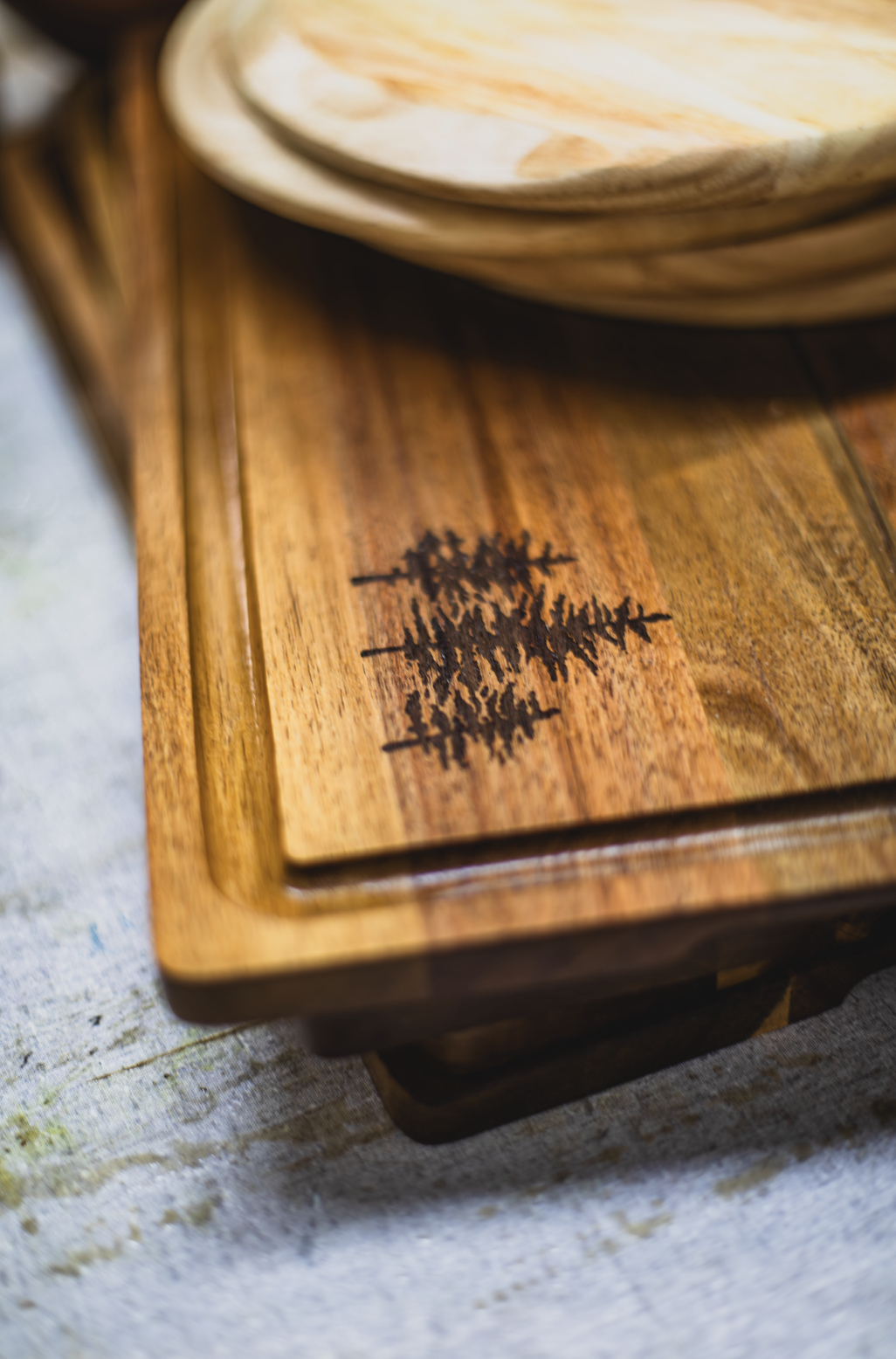 Close-up of a wooden cutting board with a forest silhouette design, placed on a wooden table.