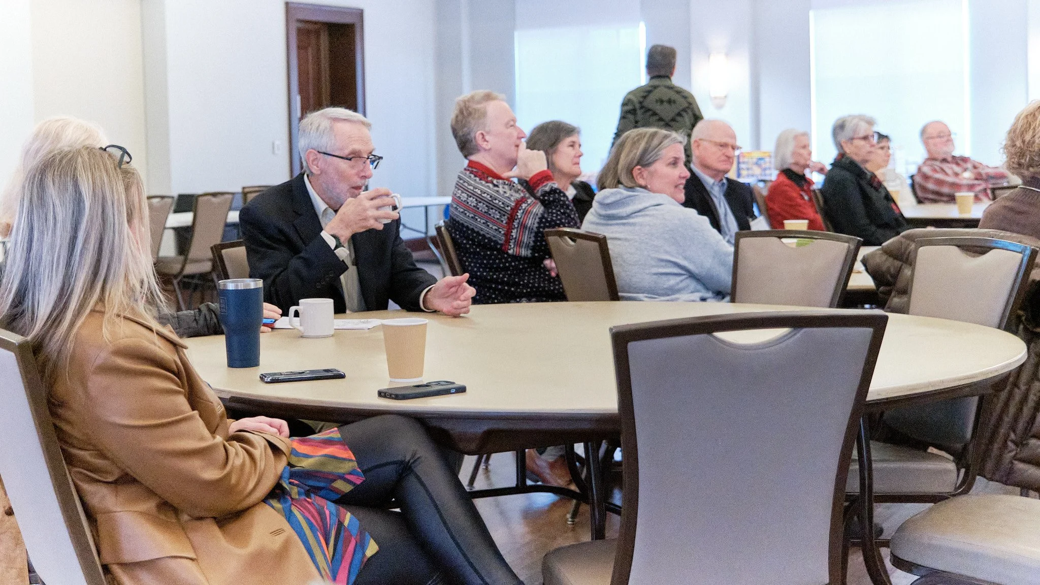 People attending a meeting or seminar seated around a large table in a well-lit room.