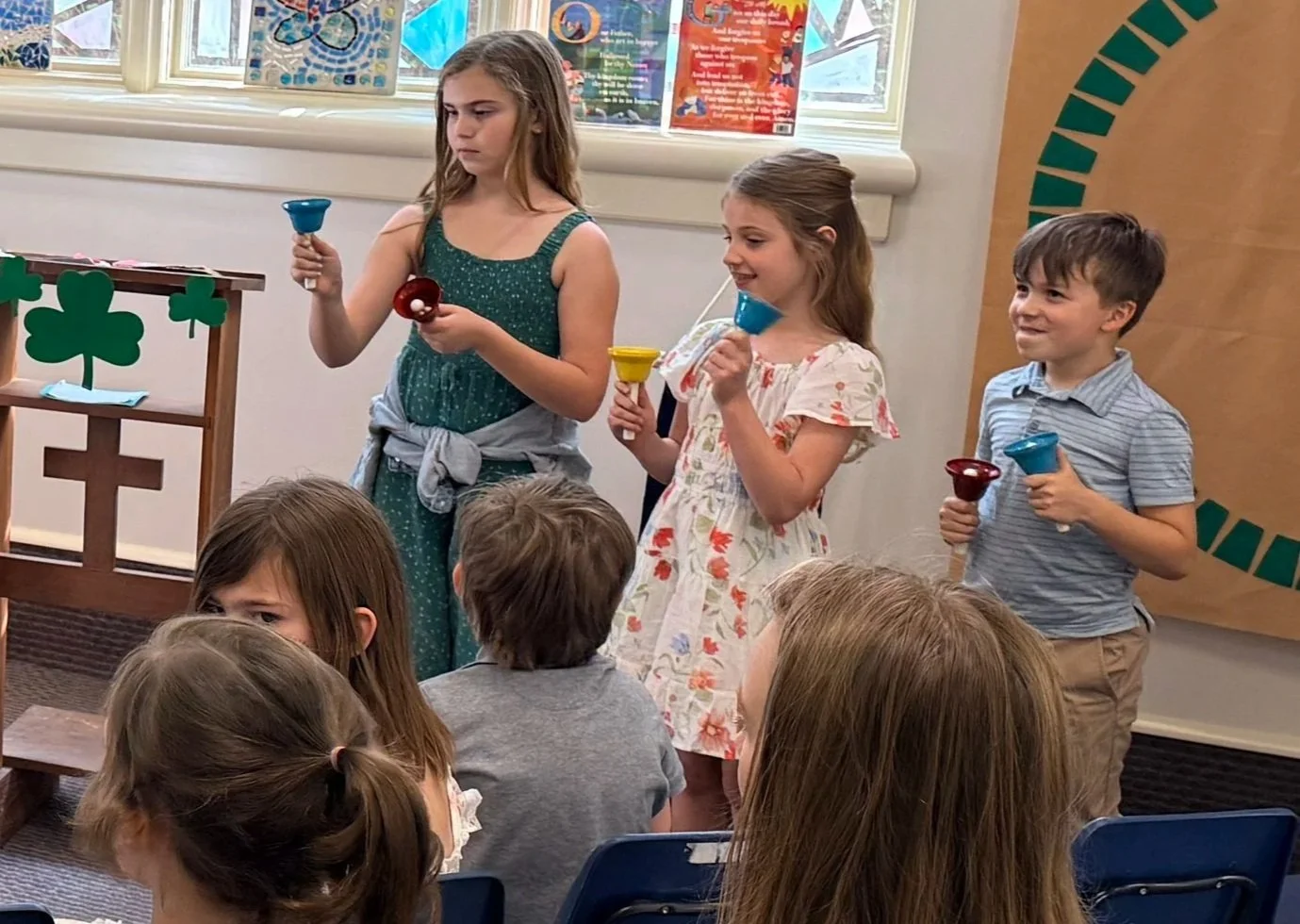 Children standing and sitting in a classroom, participating in a game or activity involving colorful plastic cups.