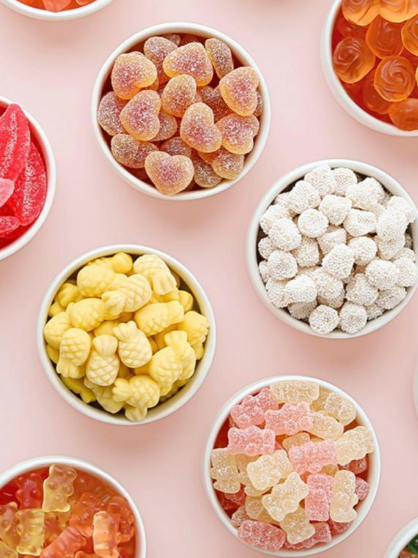 Various bowls of gummy candies in different shapes and colors on a pink surface.