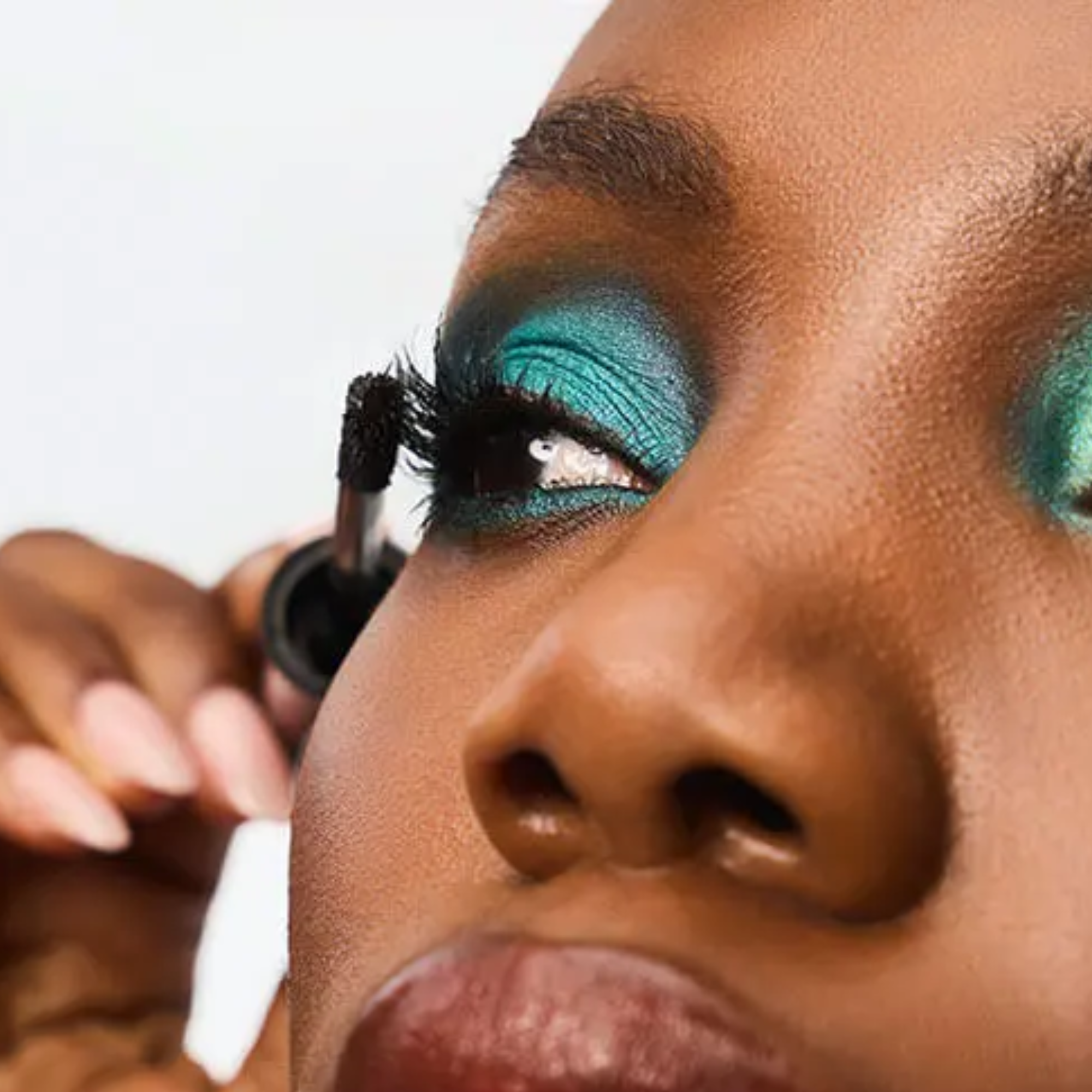 Close-up of a woman applying turquoise eyeshadow with a makeup brush.