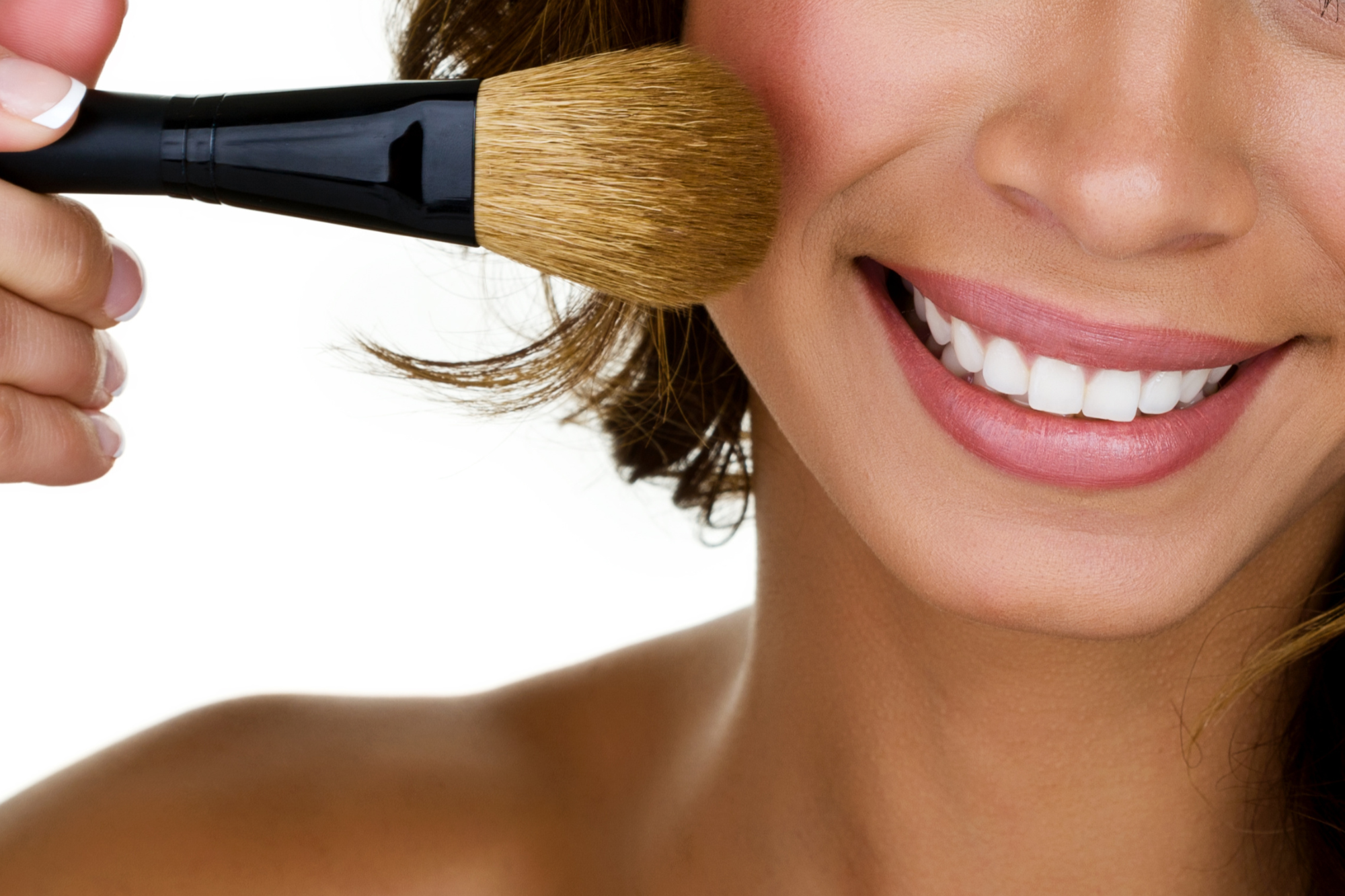 A woman smiling as she applies makeup with a large makeup brush.