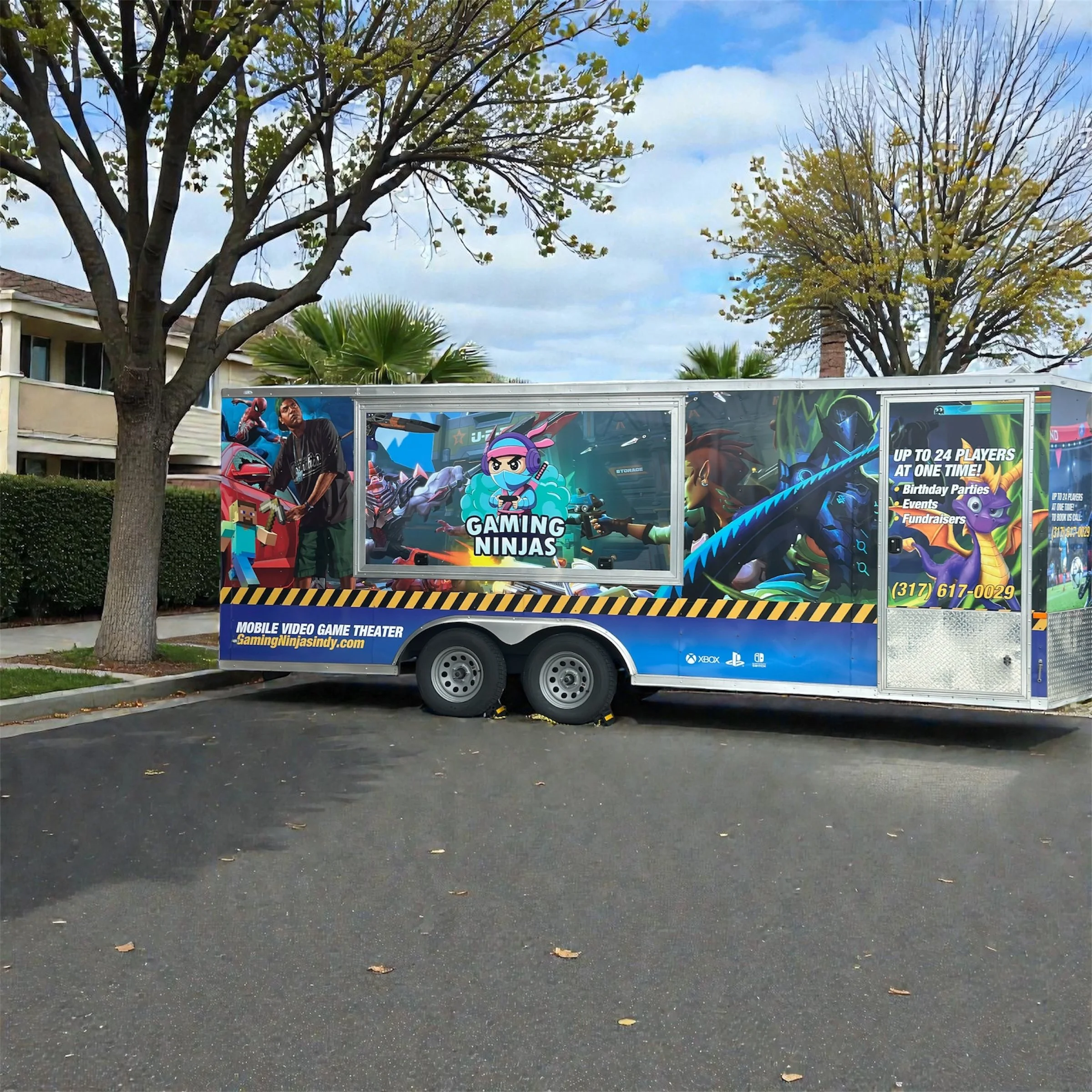 A mobile video game theater trailer parked in Hancock County Indiana on a street, decorated with gaming-themed banners and artwork featuring characters from popular video games, advertising event services for gaming parties and fundraisers.