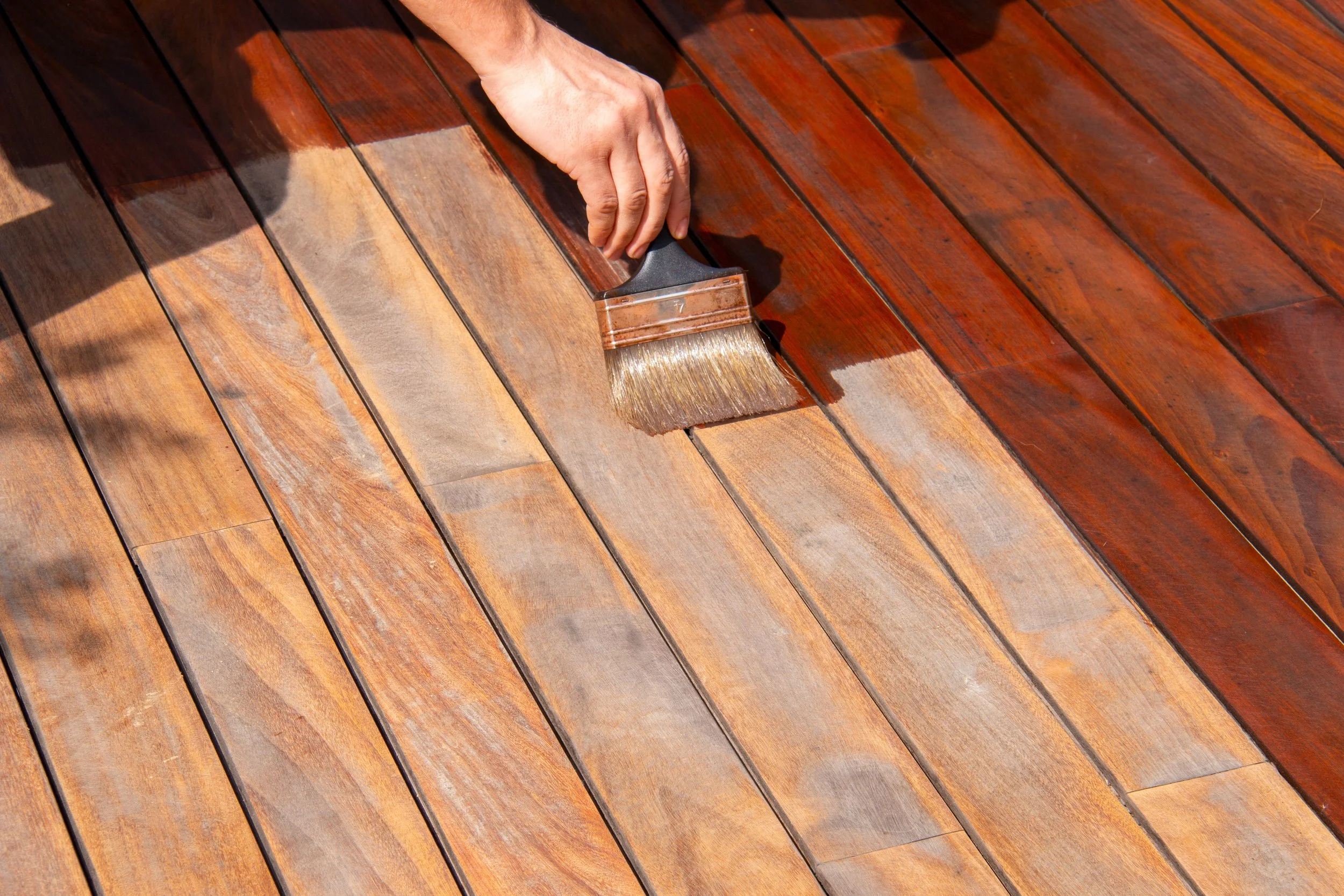 A person applying stain to a wooden deck with a brush.