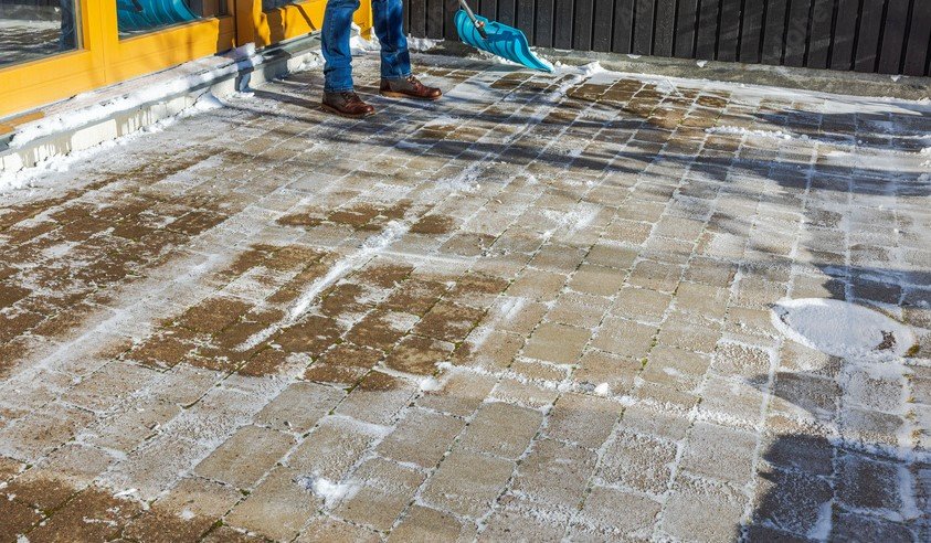 Person cleaning snow and ice from paved brick patio with a snow shovel.
