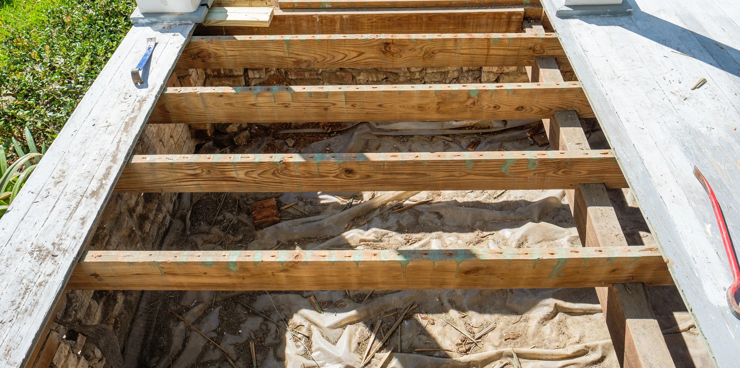 Wooden staircase frame under construction, with weathered white wooden side rails and scaffolding on a construction site.