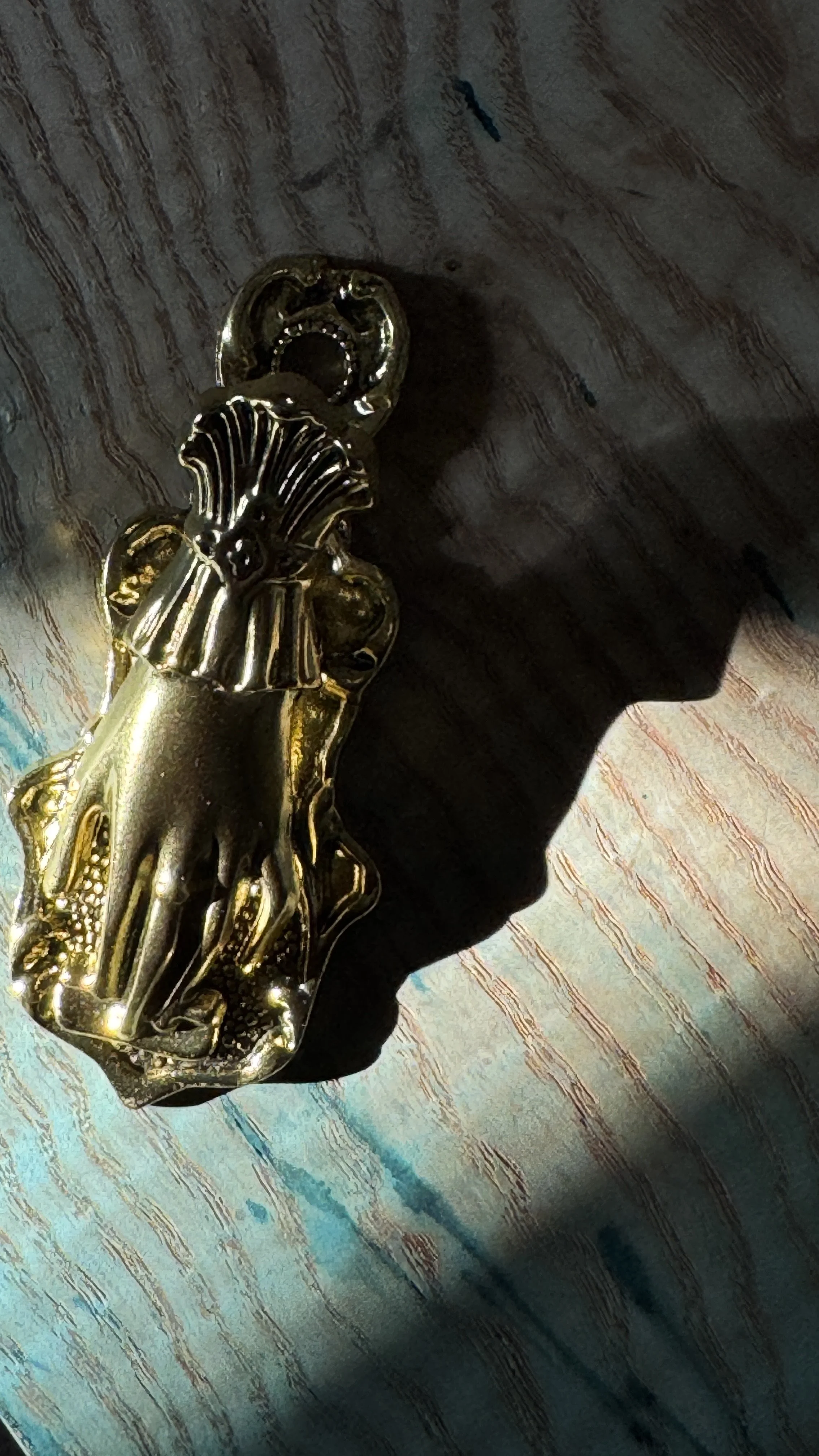 A gold-colored decorative object resembling a hand is placed on a textured wooden surface, casting a shadow to the right.